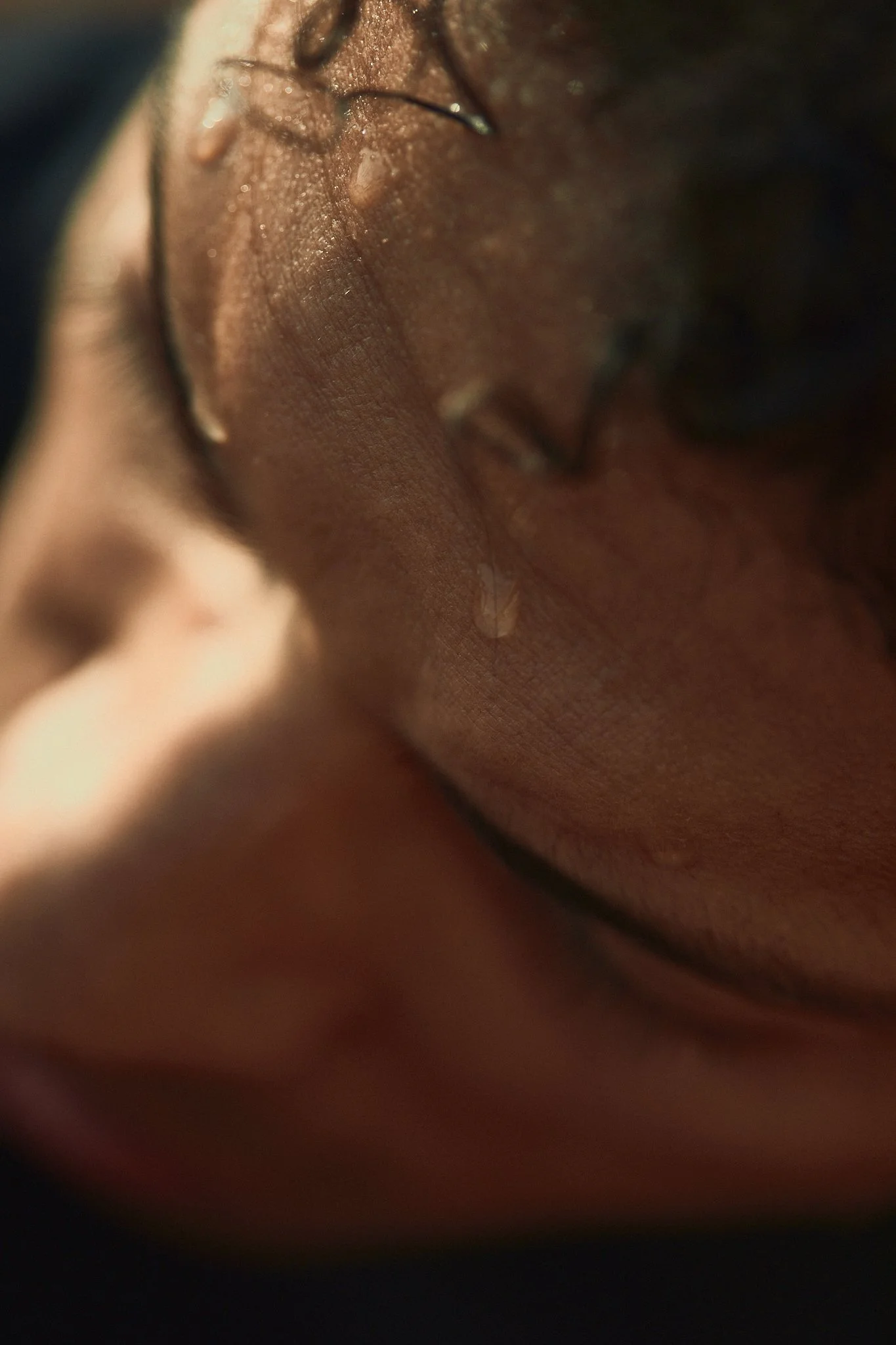 Close-up of a wet, textured skin on a person’s face, with water droplets and strands of curly hair.