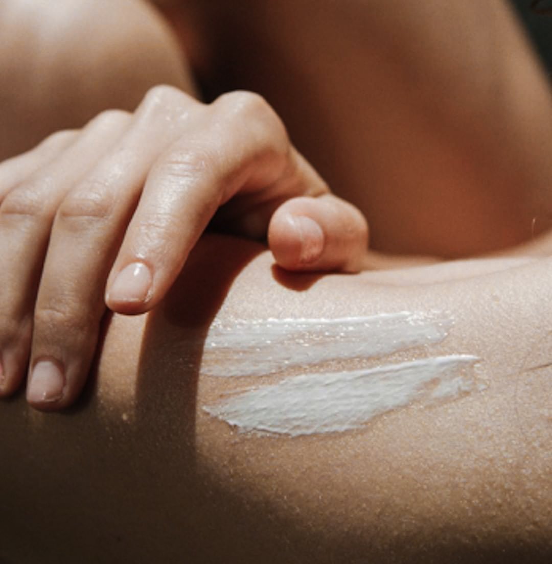 Close-up of a person applying white cream or lotion to their shoulder using their finger.