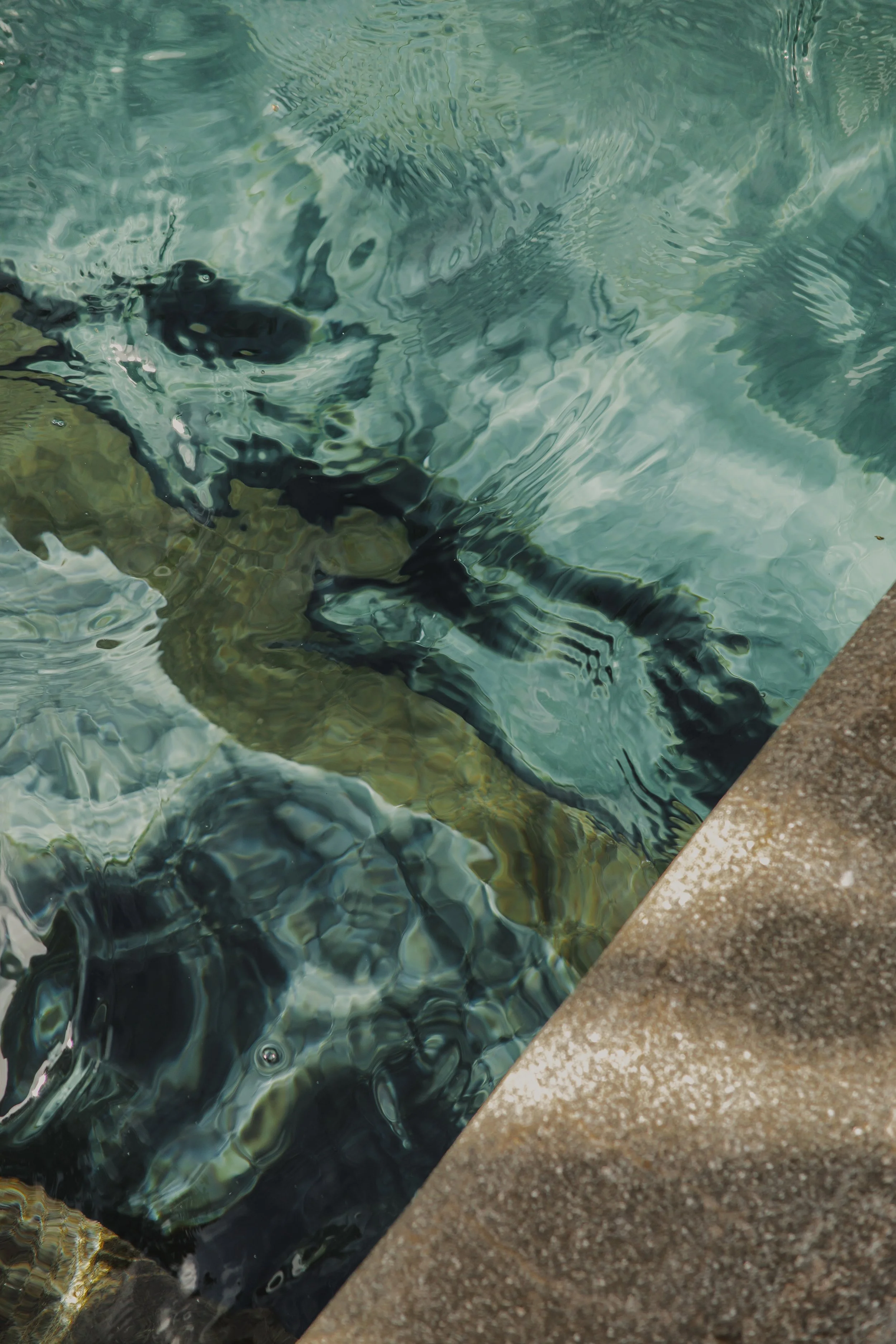 Close-up view of water with ripples and a concrete edge of a pool.