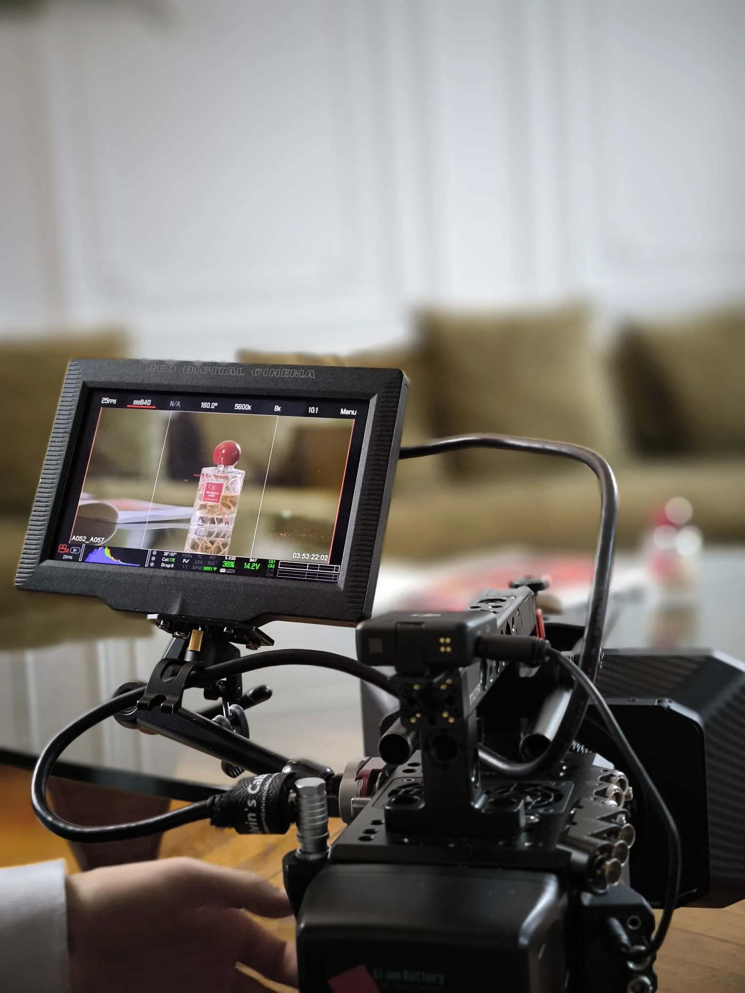 Close-up of a camera monitor mounted on a camera rig, displaying a shot of a perfume bottle with a red cap.