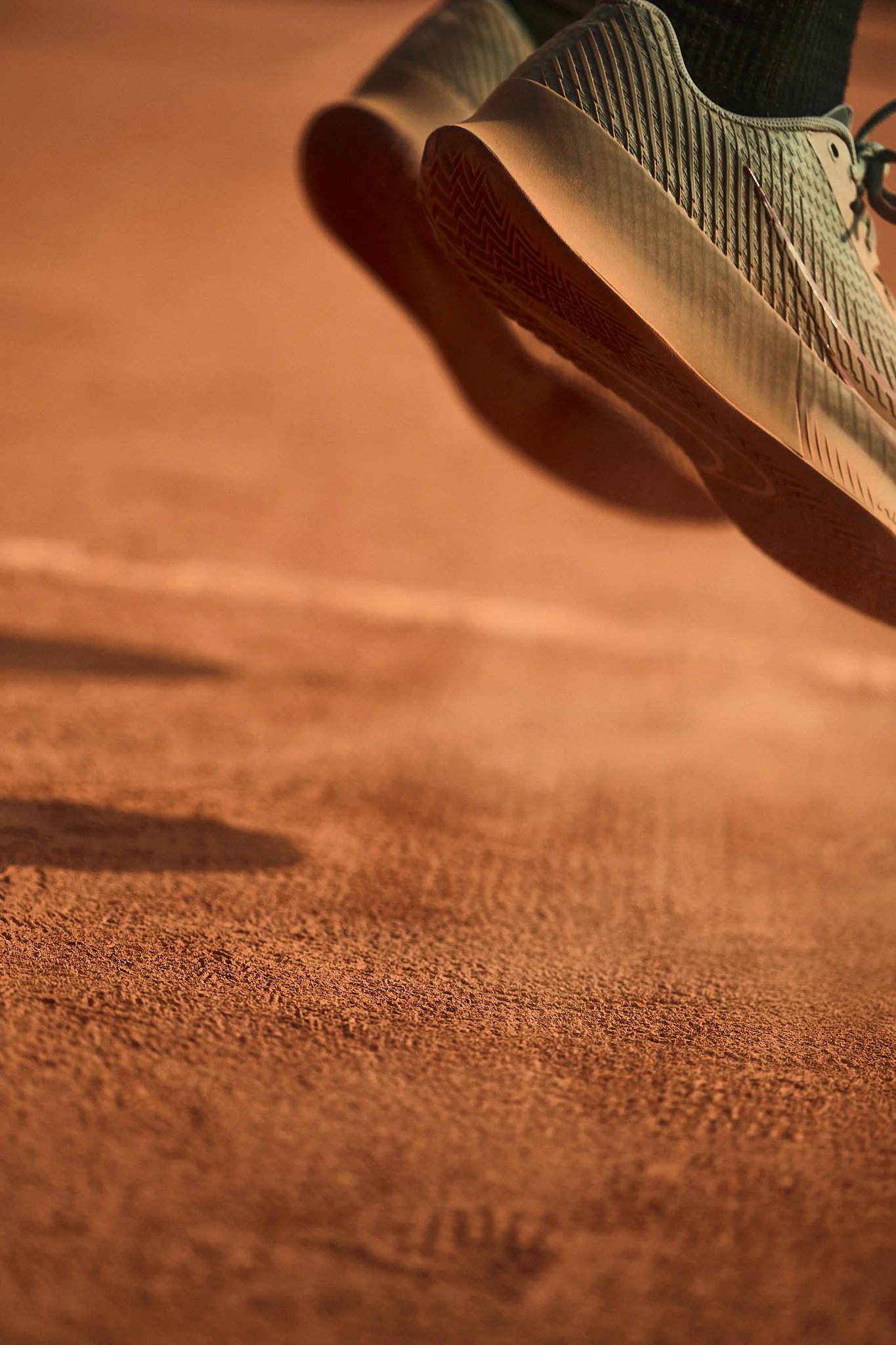 Close-up of a sneaker on a clay court surface, with the focus on the sole and side of the shoe.