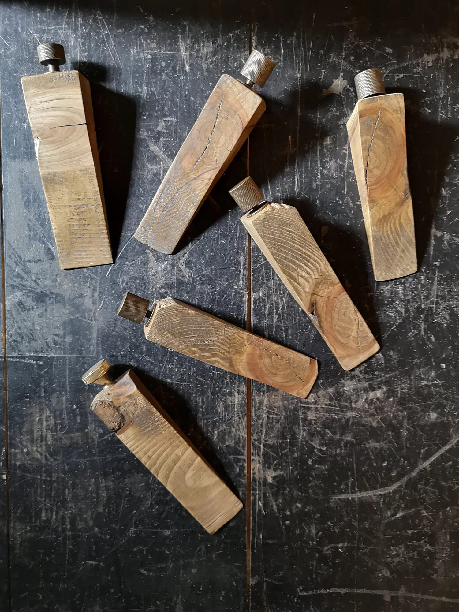 Several large, irregular-shaped wooden blocks with knurled metal knobs on top are arranged on a dark, scratched floor.