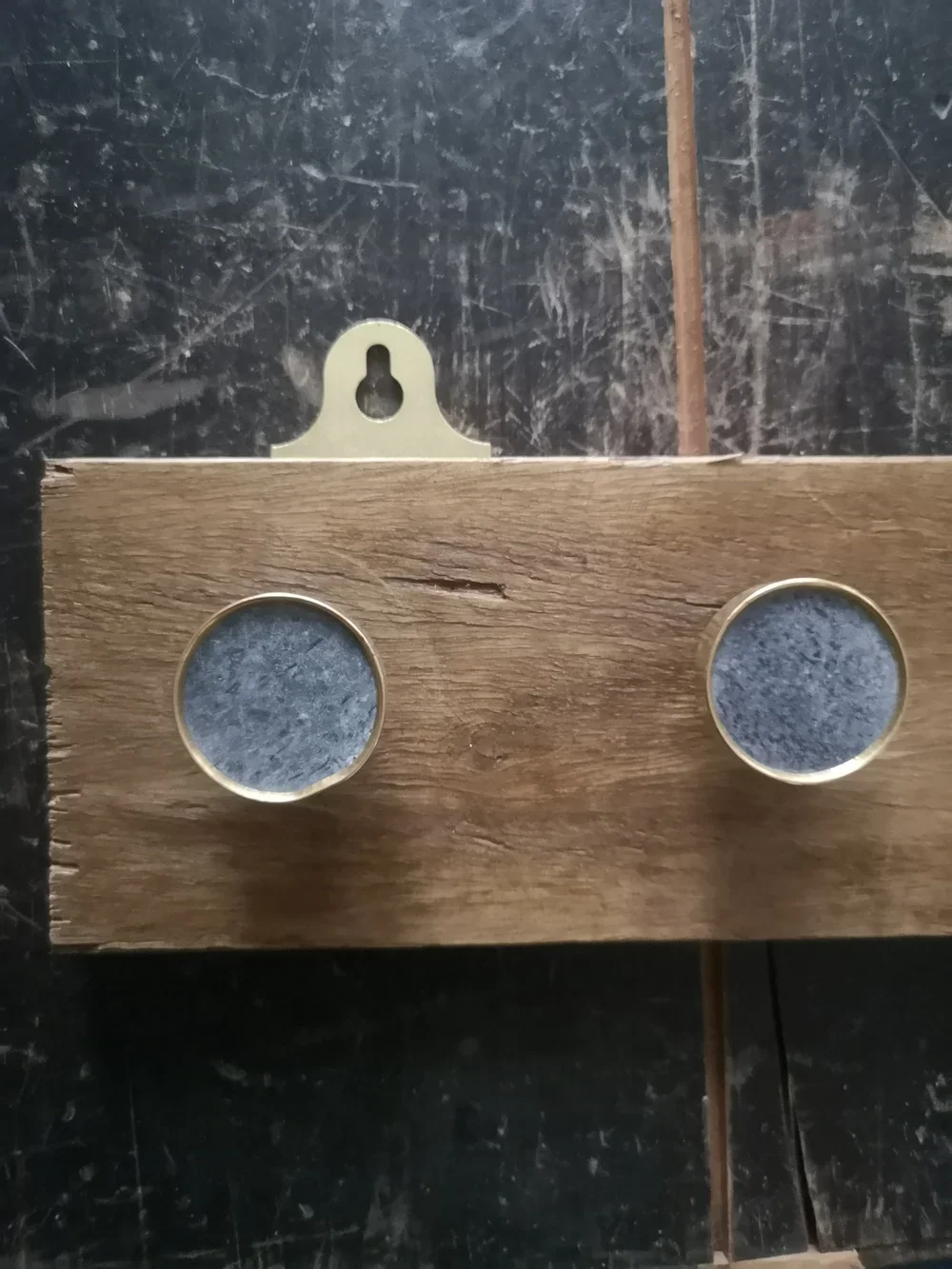 Wooden piece with two round holes and a metal bracket with an oval hole attached on a black scratched surface.