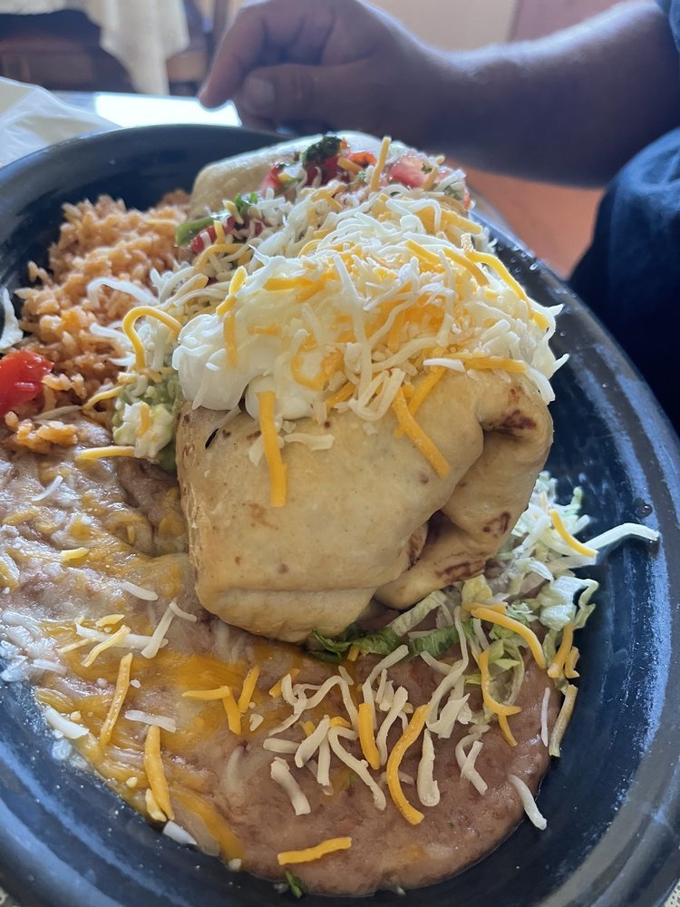 Plate with stuffed burrito topped with shredded cheese, side of rice with cheese and tomato, and refried beans with shredded cheese.