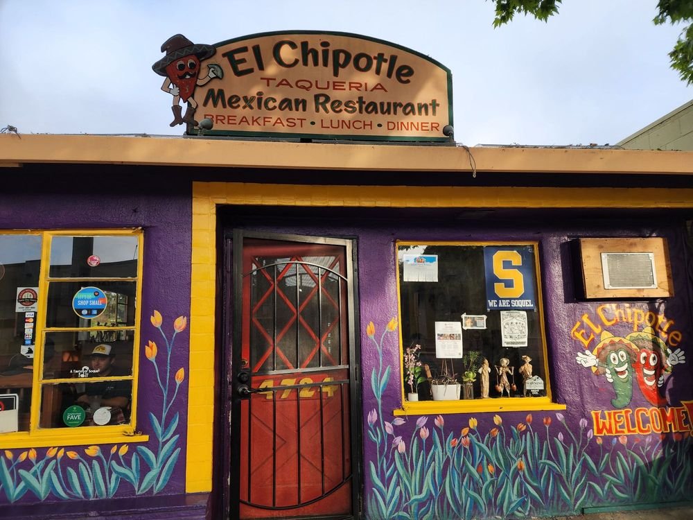 Colorful exterior of El Chipotle Mexican Restaurant with purple and yellow decorations, painted flowers, and a cartoon chili pepper mascot.