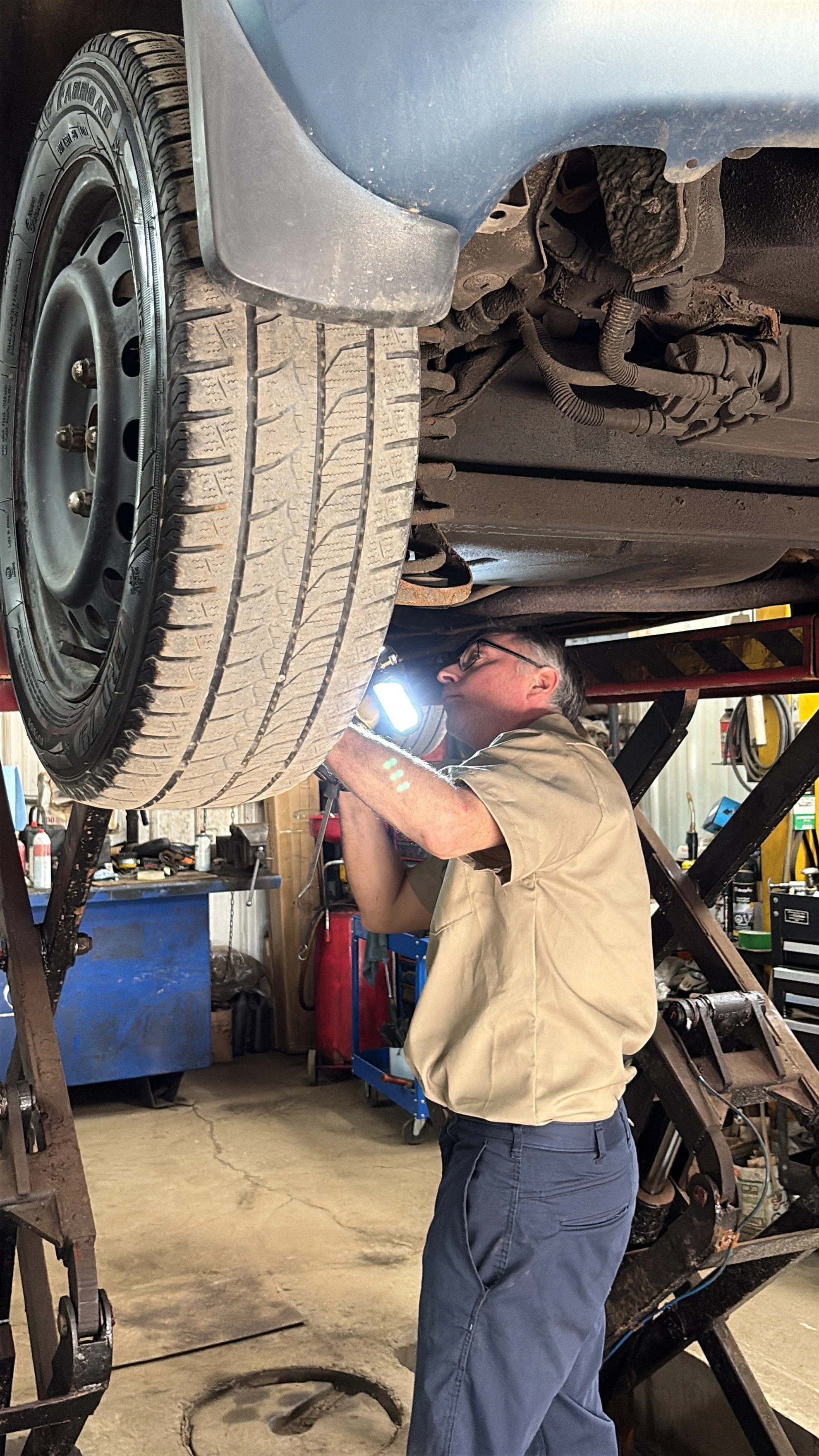 Un mécanicien inspecte ou travaille sur le dessous d'une voiture suspendue sur un pont élévateur dans un atelier de réparation automobile.