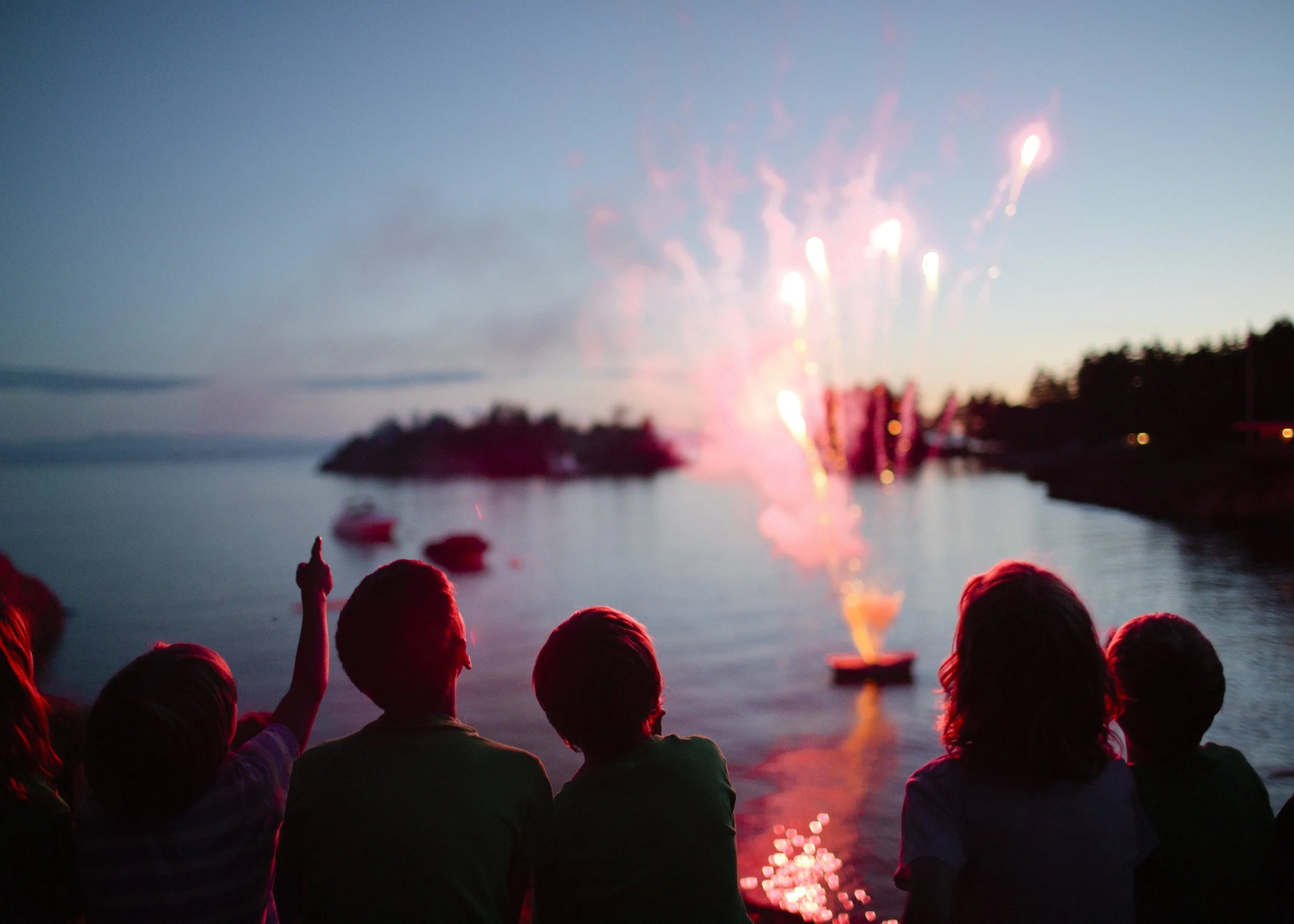 A group of children watching fireworks over a body of water during dusk.