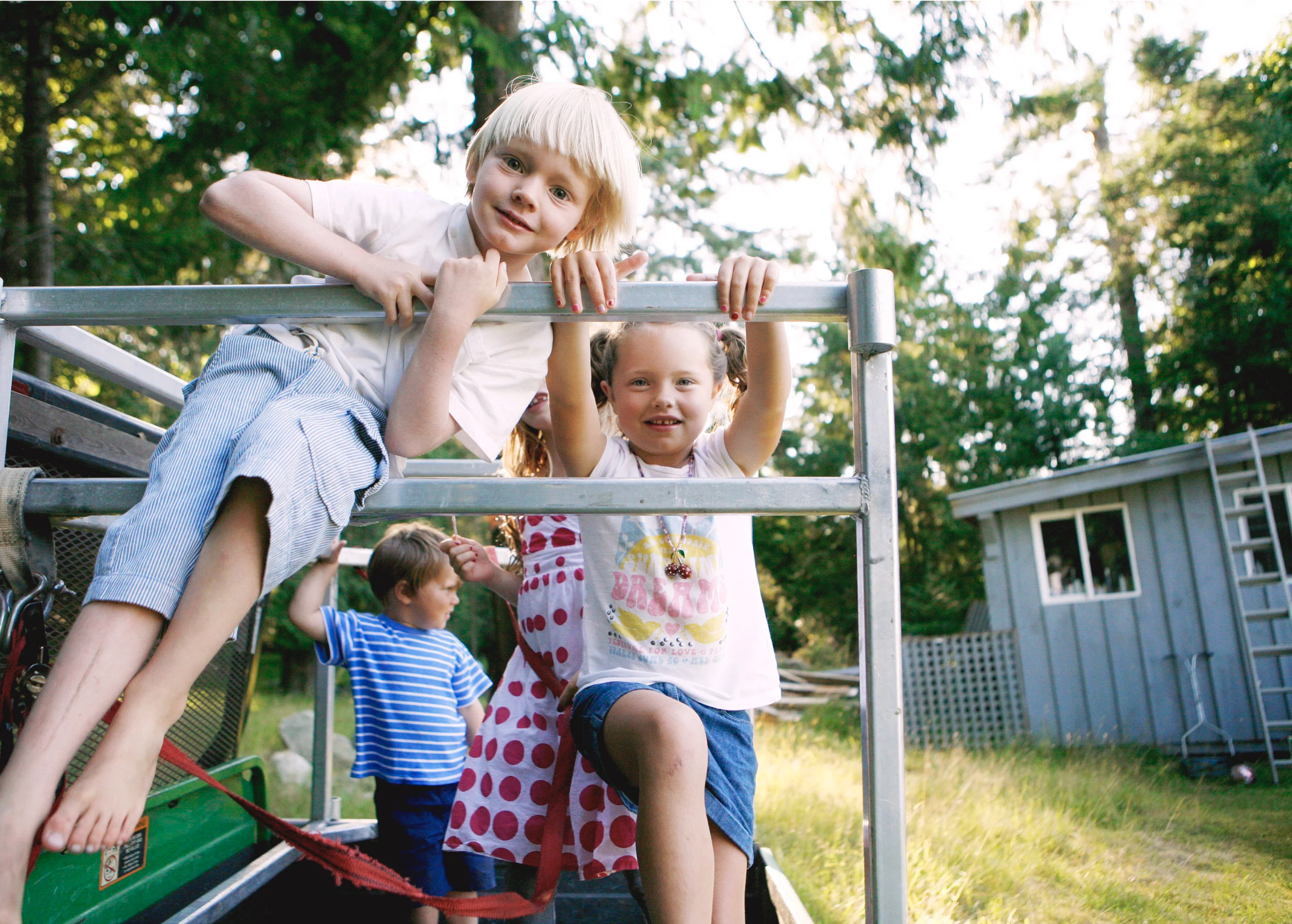 Children playing on a playground slide outdoors surrounded by trees and a house in the background.