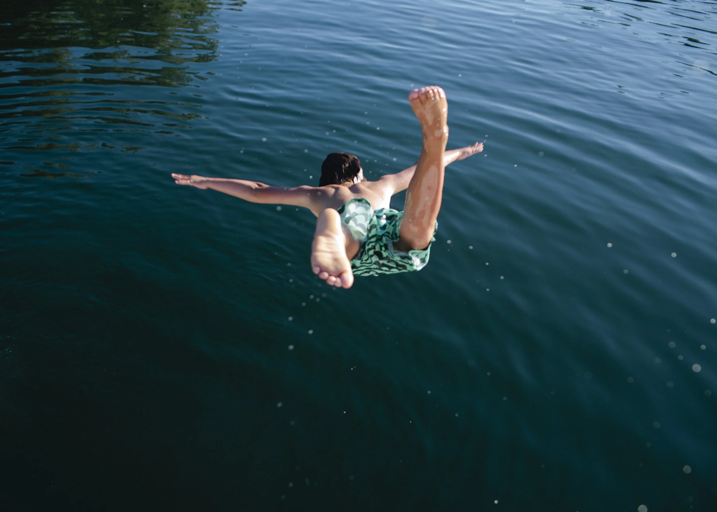A person swimming in a body of water, viewed from behind, with water splashing around.
