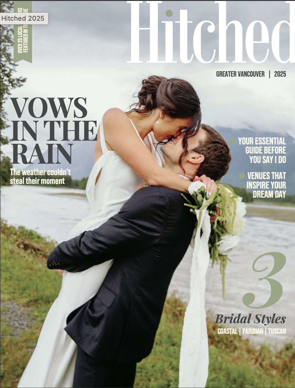 A couple, a woman and a man, in wedding attire sharing a romantic moment outdoors near a river, with mountains in the background. The woman is being lifted by the man, and they are close to kissing, with the woman holding a bouquet of white flowers.