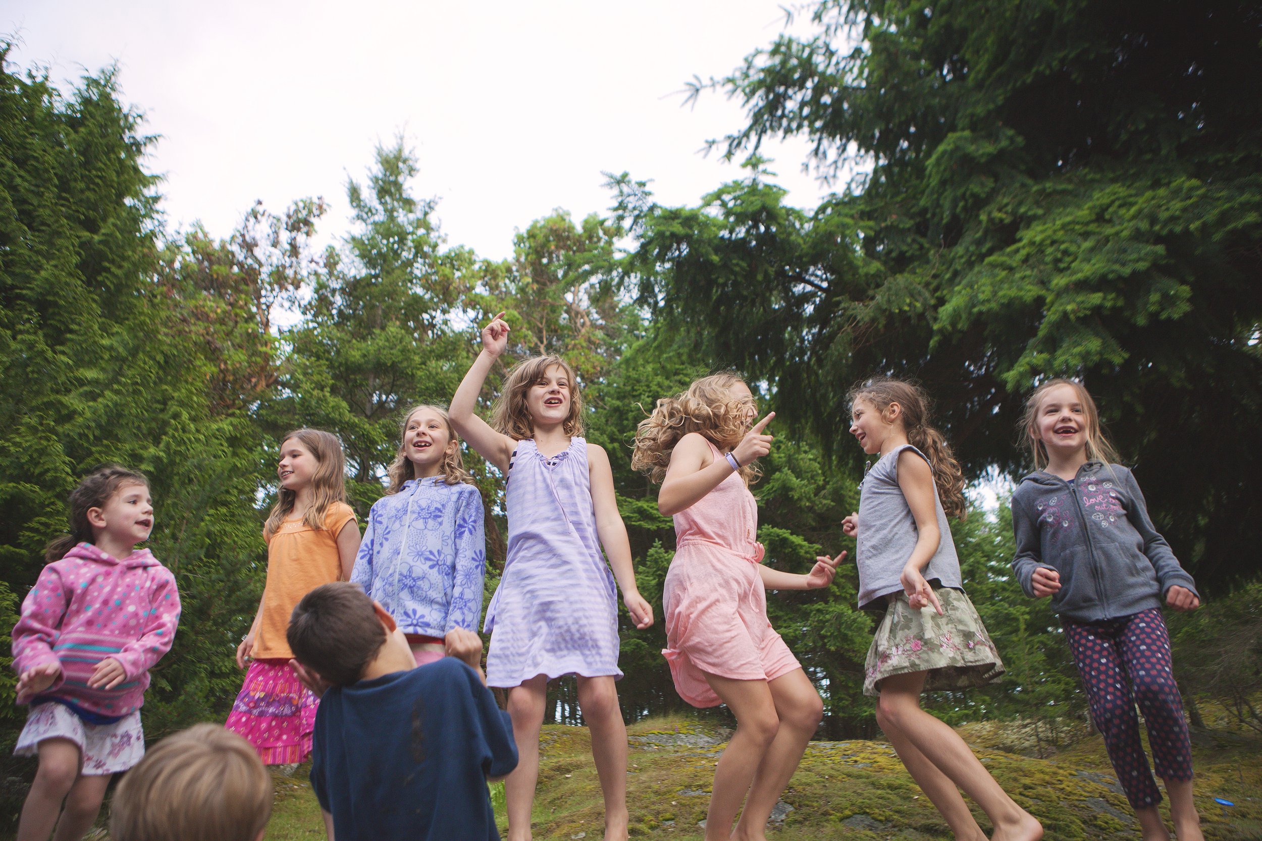 A group of children playing outdoors in a park surrounded by trees, smiling and interacting with each other.