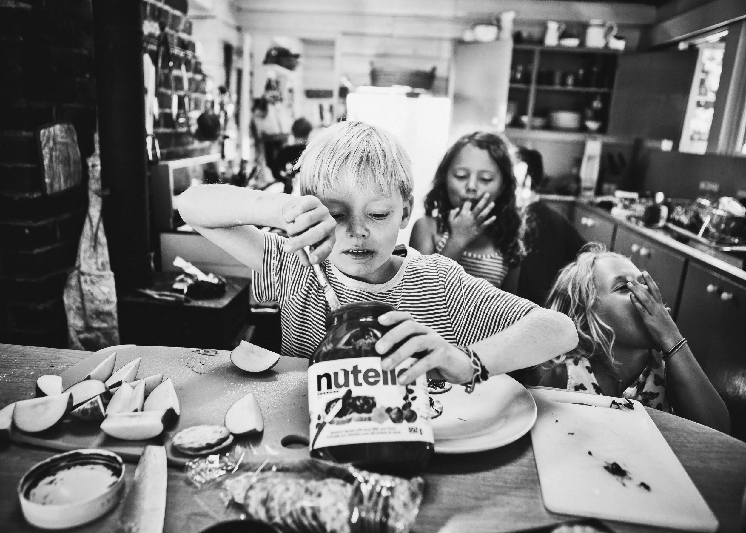 Children at a table with watermelon slices, Nutella spread, and snacks in a cozy kitchen or dining area.