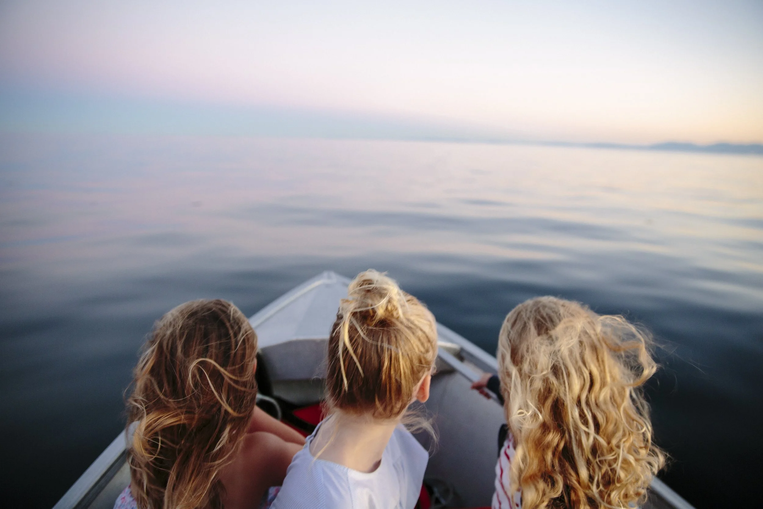 View of the ocean from the back of a boat with five children sitting at the front enjoying the scenery at sunset.