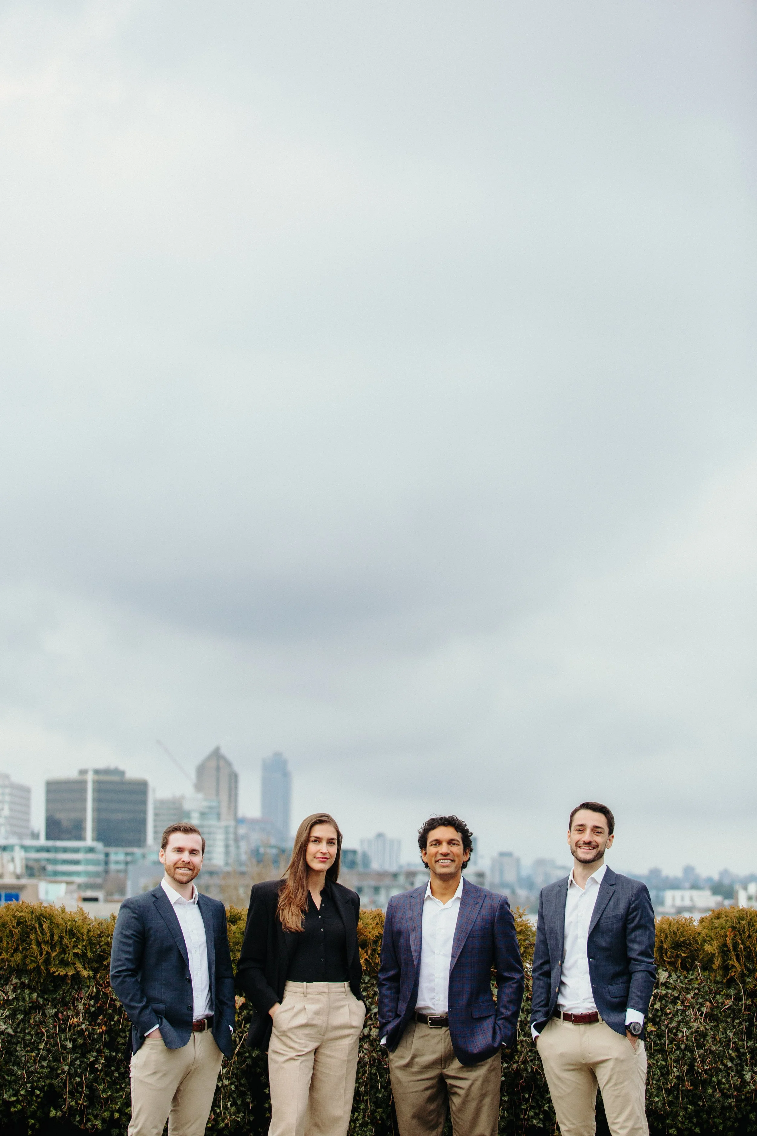 Four diverse professionals standing outdoors on a rooftop garden with city skyscrapers in the background under a cloudy sky.