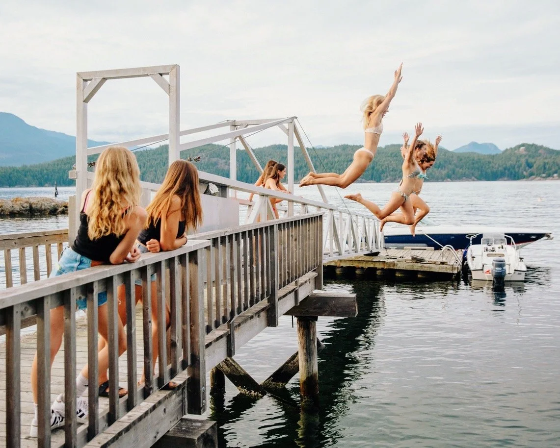 People on a dock by the water, with some jumping into the water and others watching.