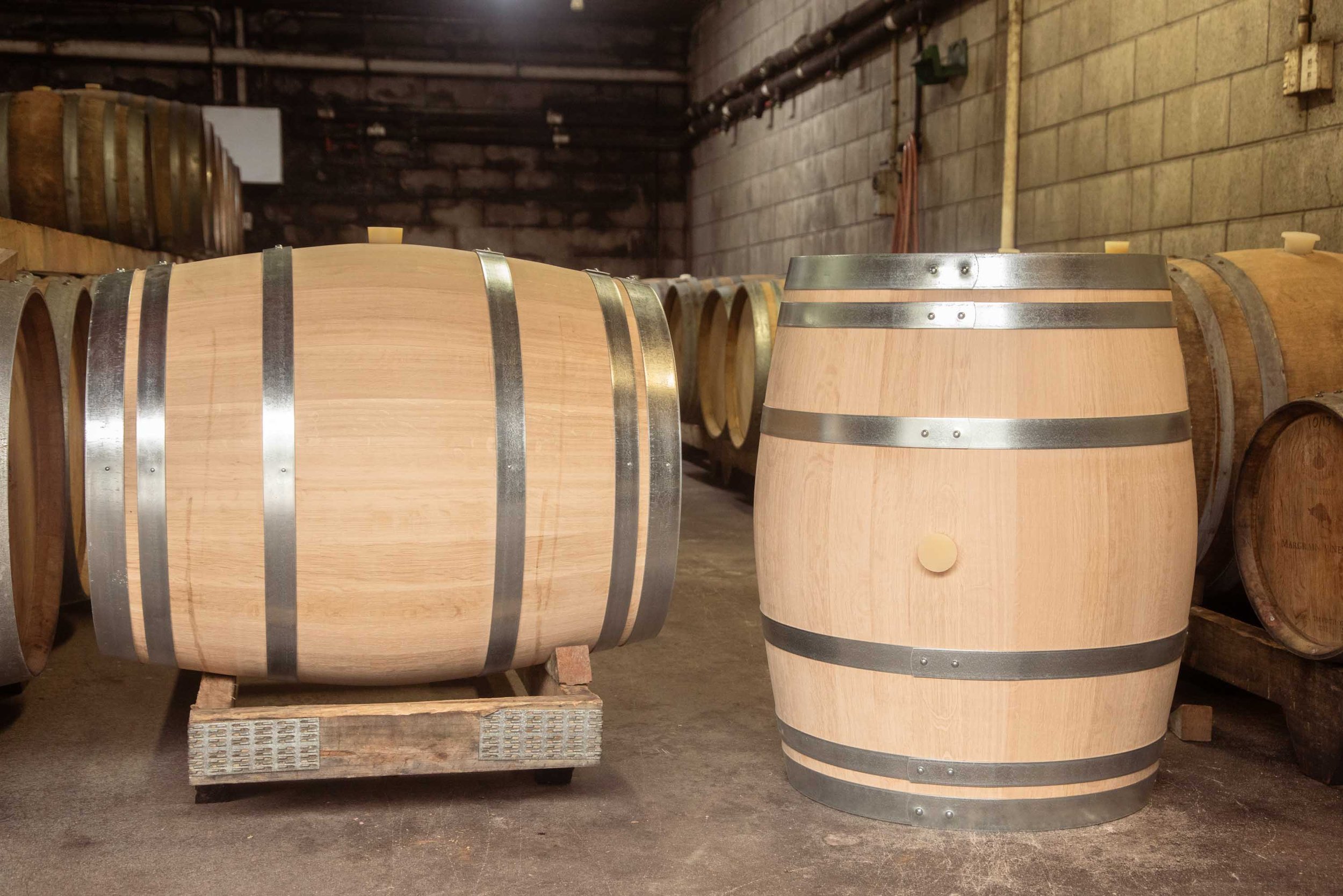 Two Barrel Co oak wine barrels in winery storage, one is laying on its side in a rack and the other is free standing