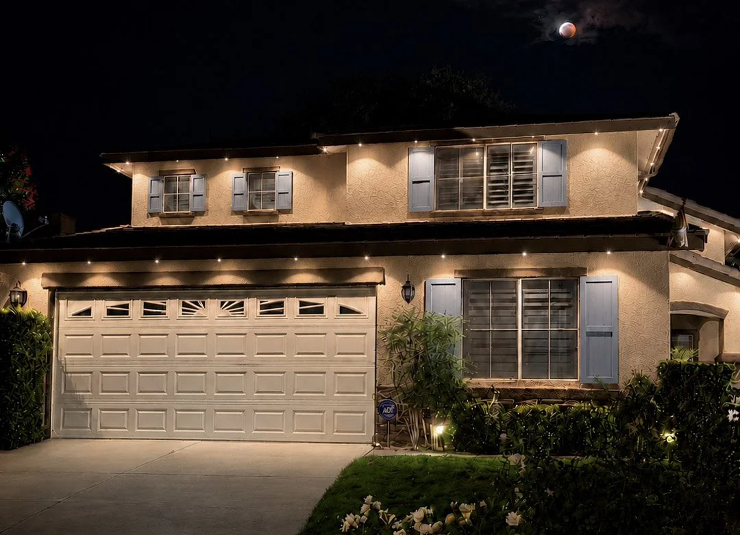 Warm white permanent LED lighting along a two-story stucco home's roofline and eaves in Los Angeles