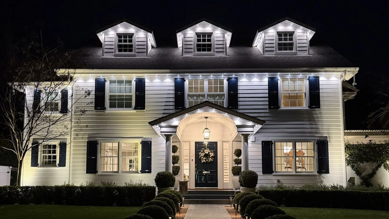 Permanent outdoor lighting installation on a Los Angeles home, with warm white LED track lighting along the roofline, dormers, and covered entryway