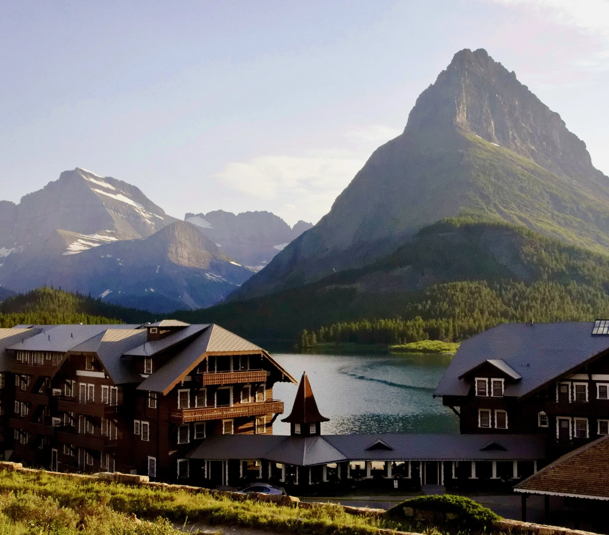 Scenic view of a lake with wooden lodging buildings in the foreground and towering mountain peaks in the background
