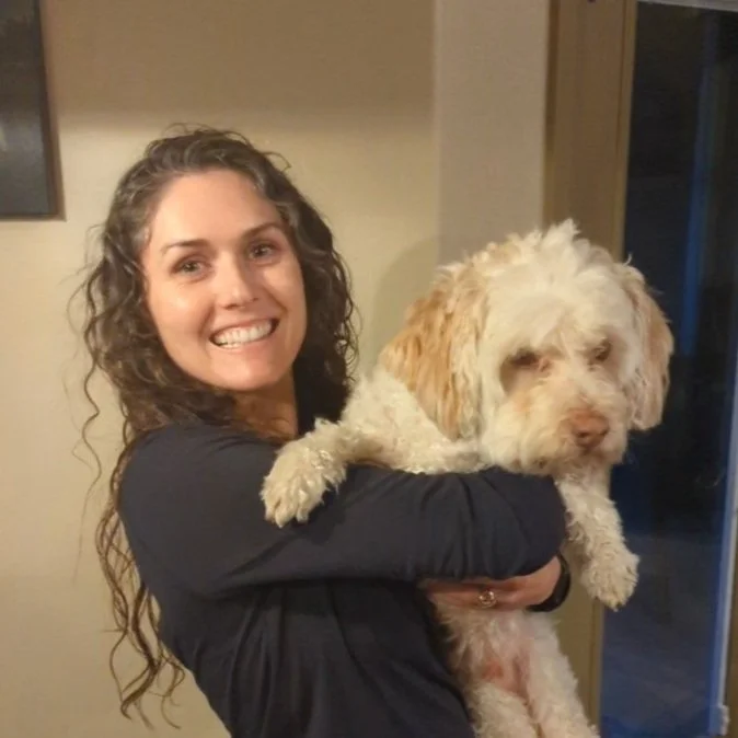 Woman with long curly brown hair holding fluffy cream dog
