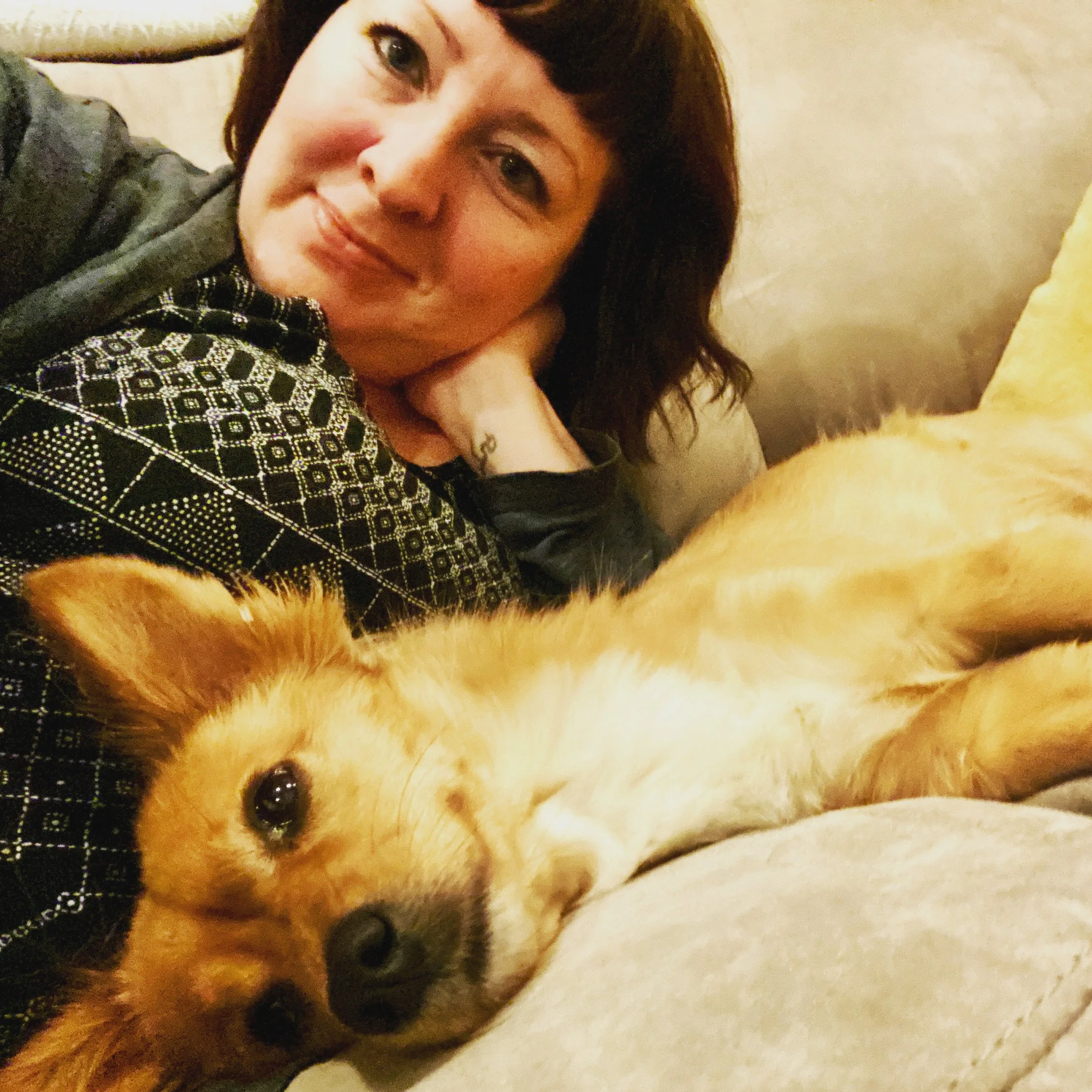 Woman with brown hair leaning on couch with gold and white dog lying in front of her