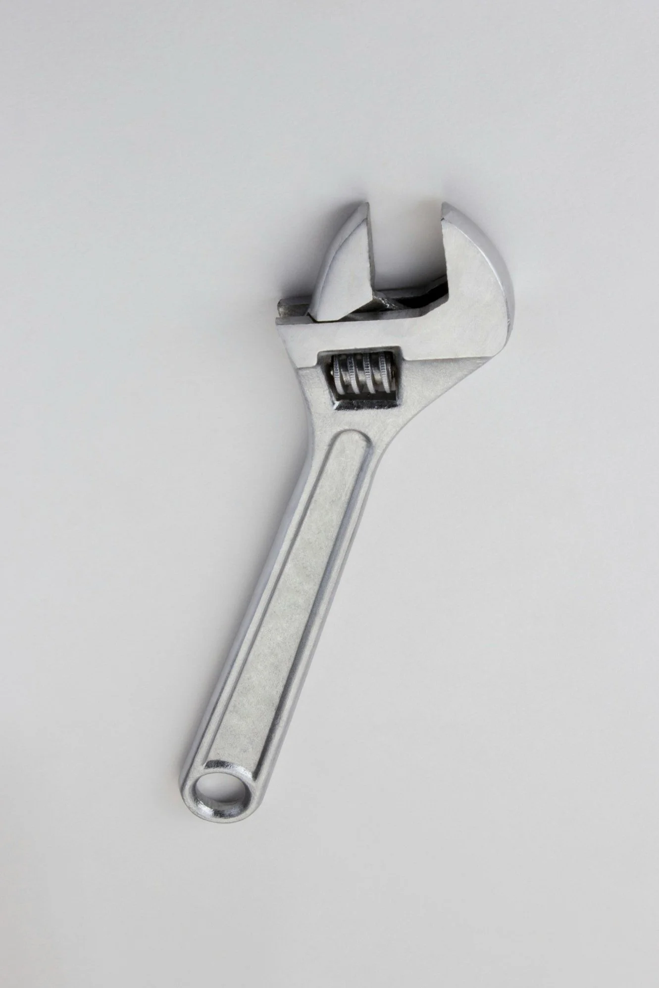 A silver adjustable wrench with its opening slightly turned against a plain light gray background.