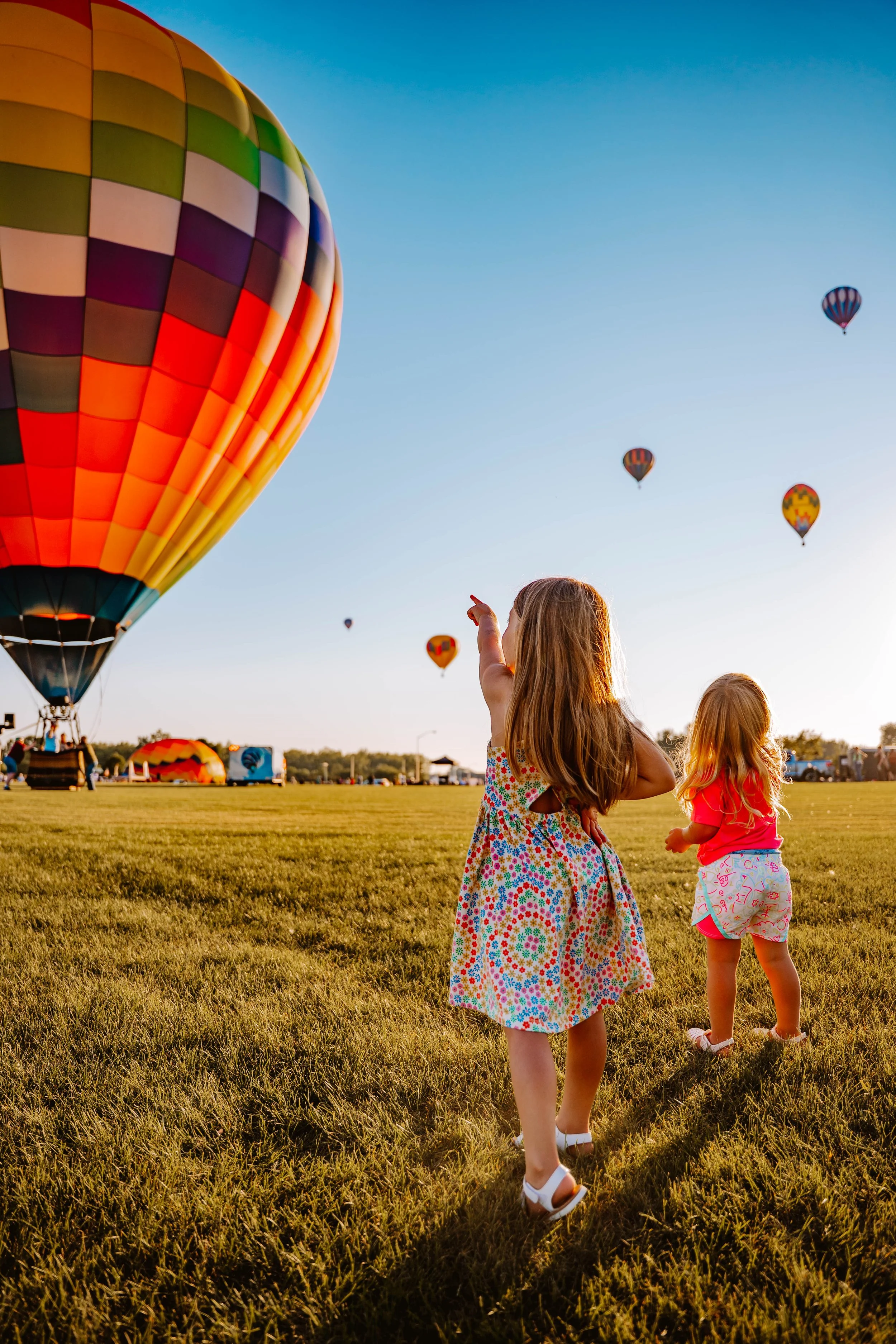Little girl pointing at hot air balloons rising into the sky.