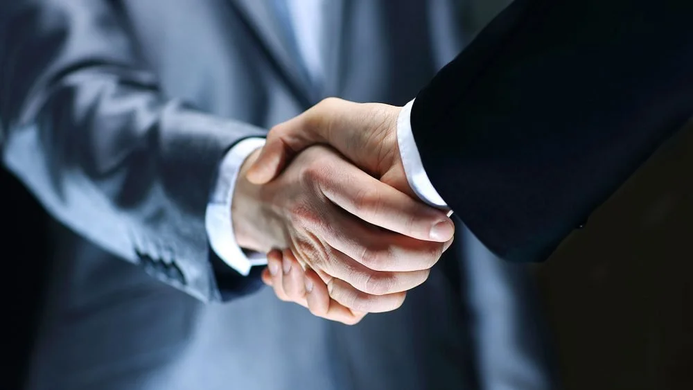Close-up of two people in business suits shaking hands.