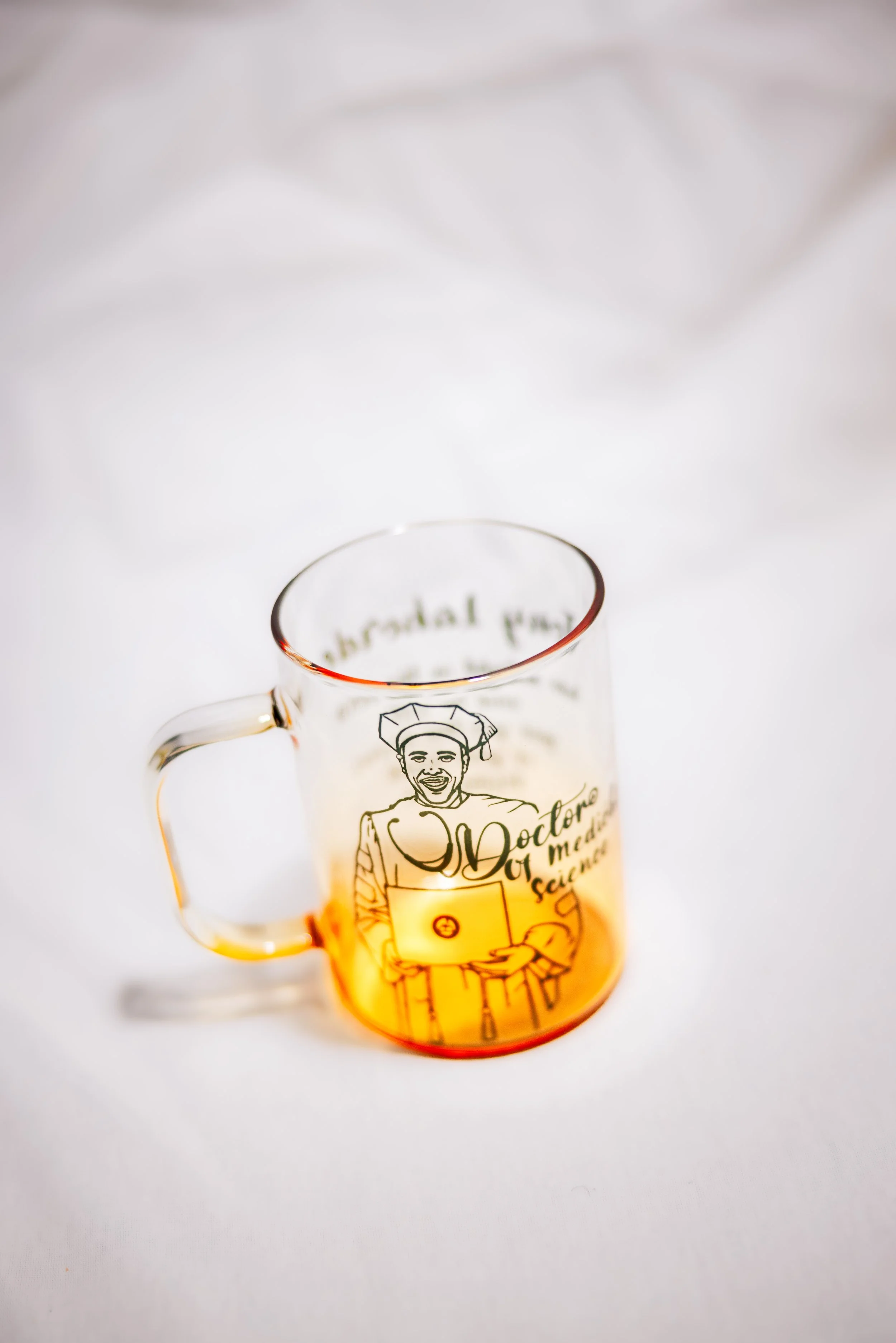 A clear glass mug featuring a cartoon image of a smiling chef with a hat, holding a spoon, surrounded by the words 'Doctor of Modern Science', placed on a white surface with a soft-focus background.