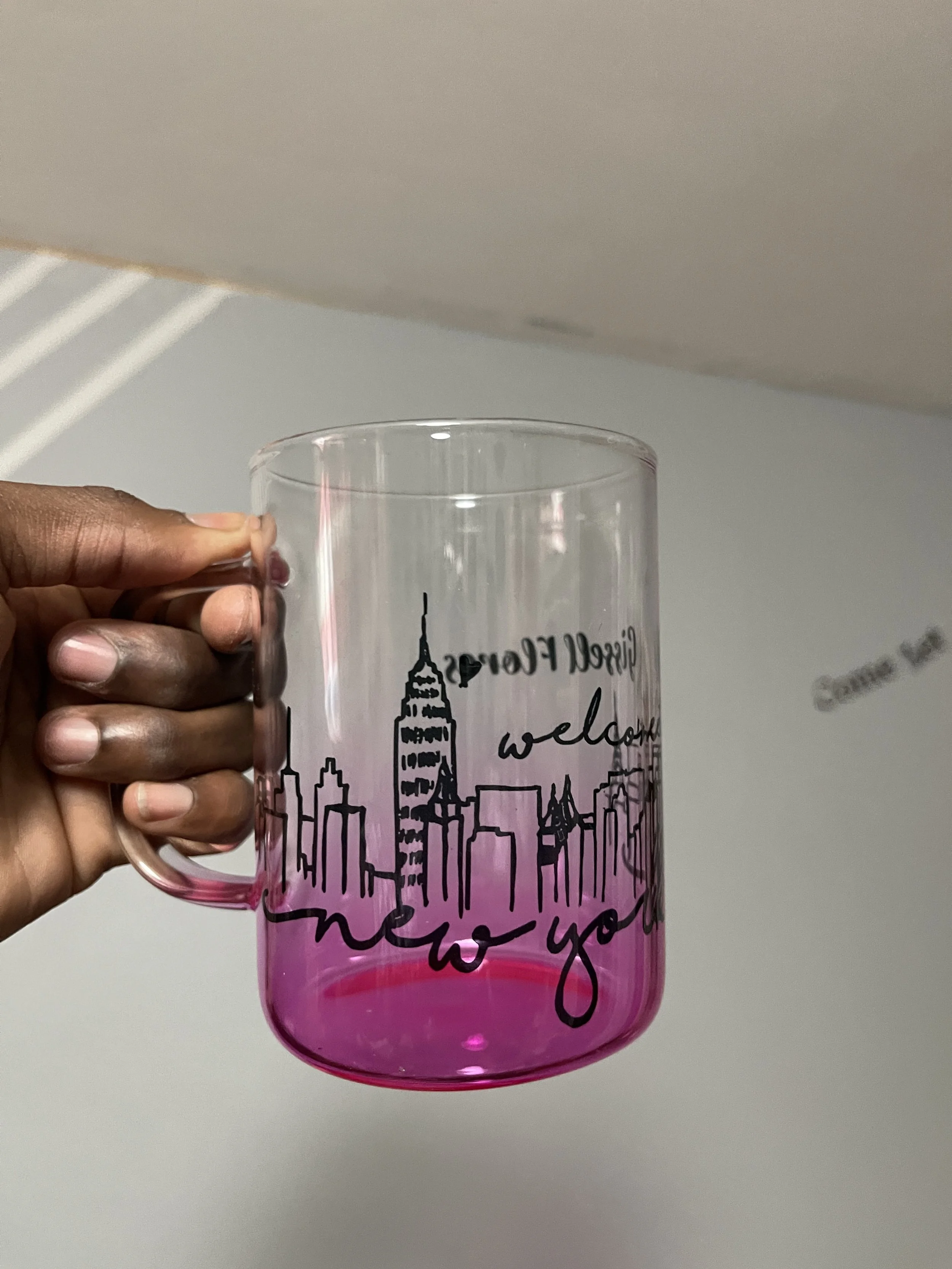 A hand holding a pink transparent plastic mug with a black city skyline design and the words 'Dream Forever' and 'welcome' printed on it.