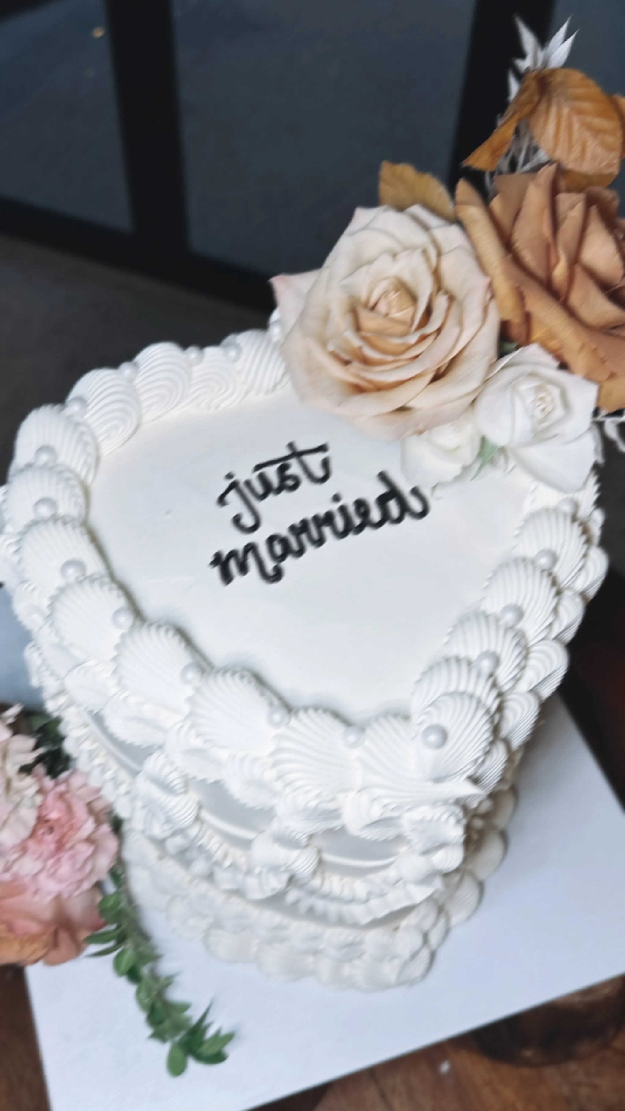 A white wedding cake with piped frosting, decorated with flowers, with the words 'just married' written on top.
