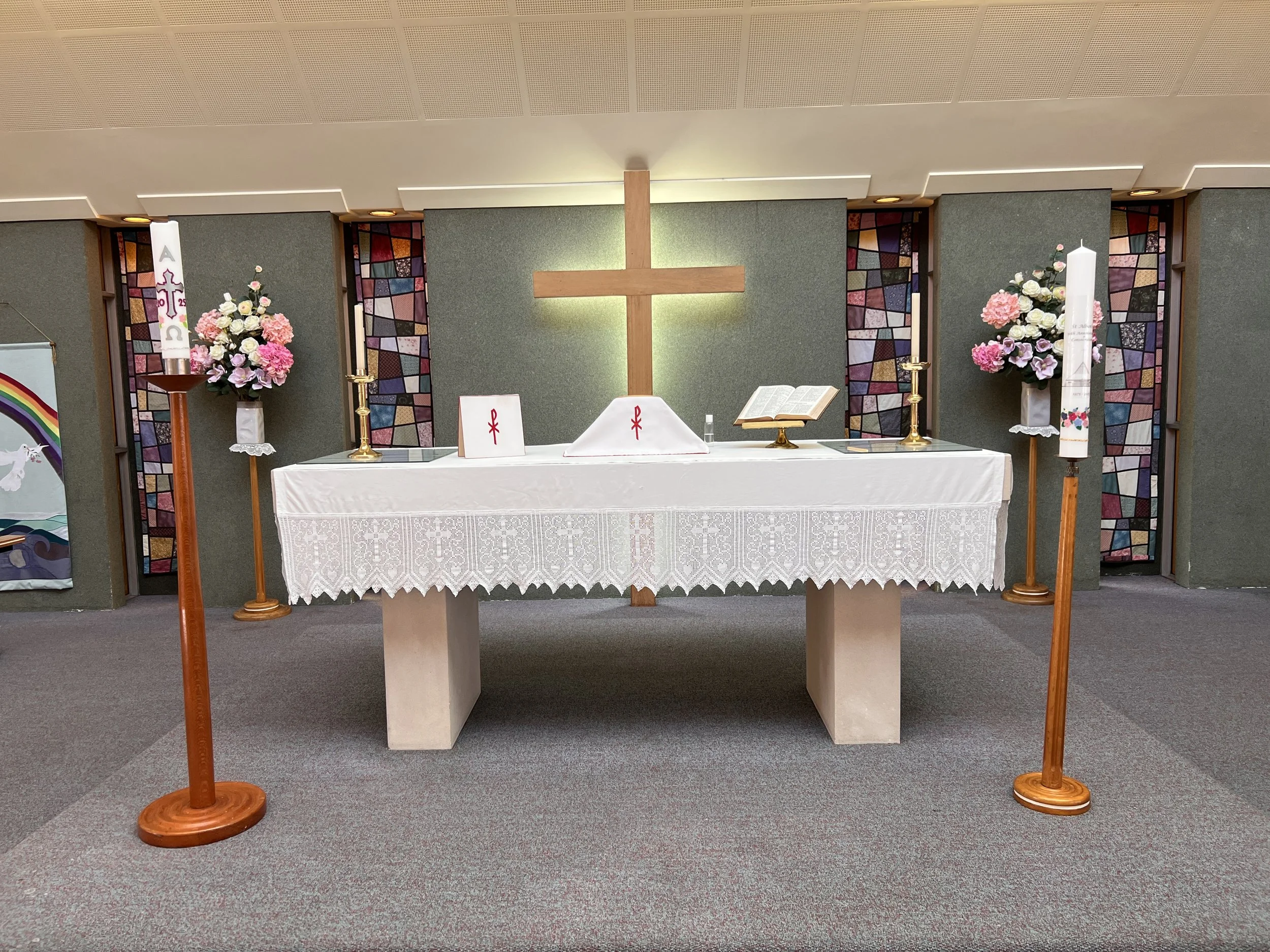 Christian altar with a wooden cross, candles, open Bible, and floral arrangements in a church interior