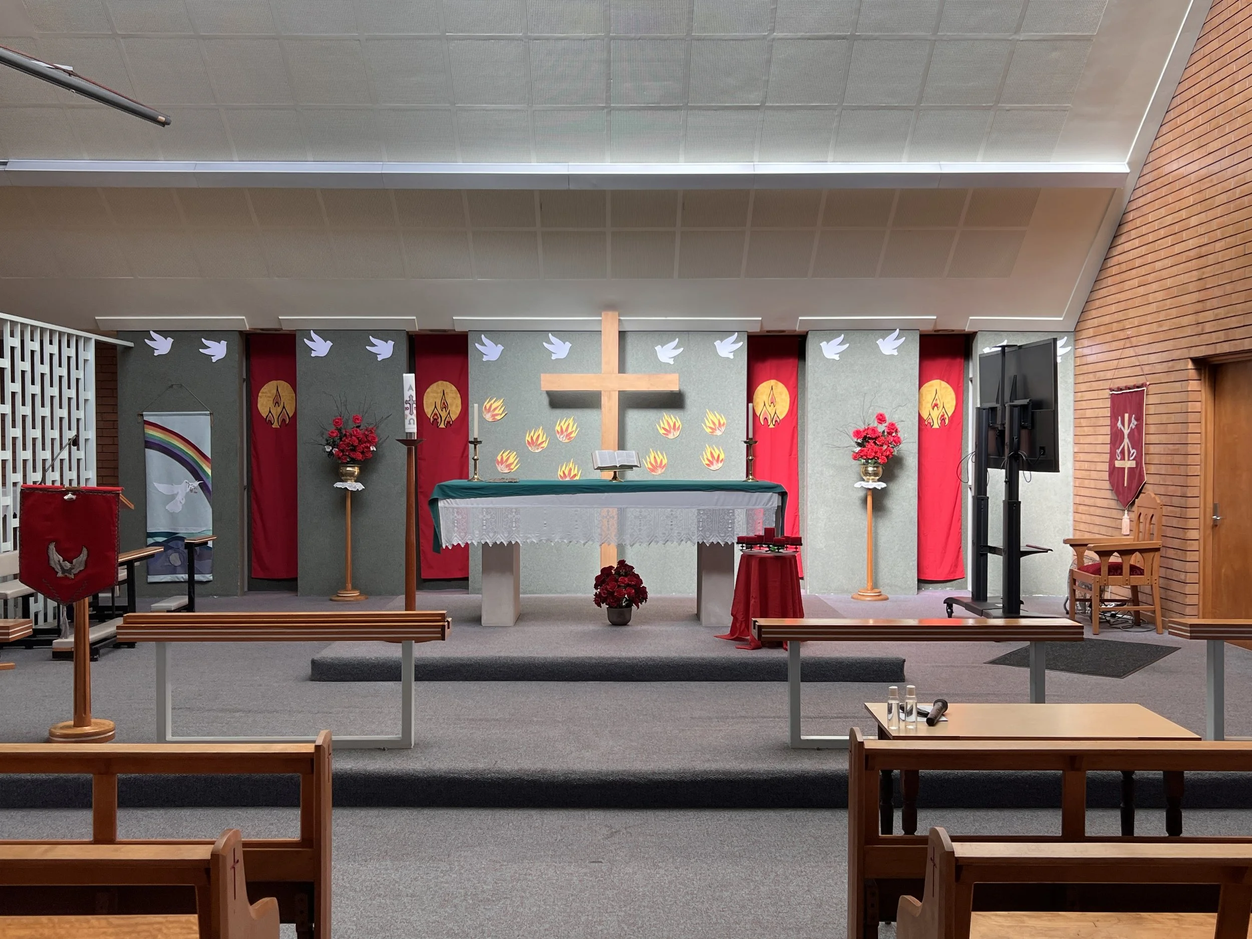 Christian altar with a large wooden cross, red and gold banners, white dove decorations, and floral arrangements, inside a church