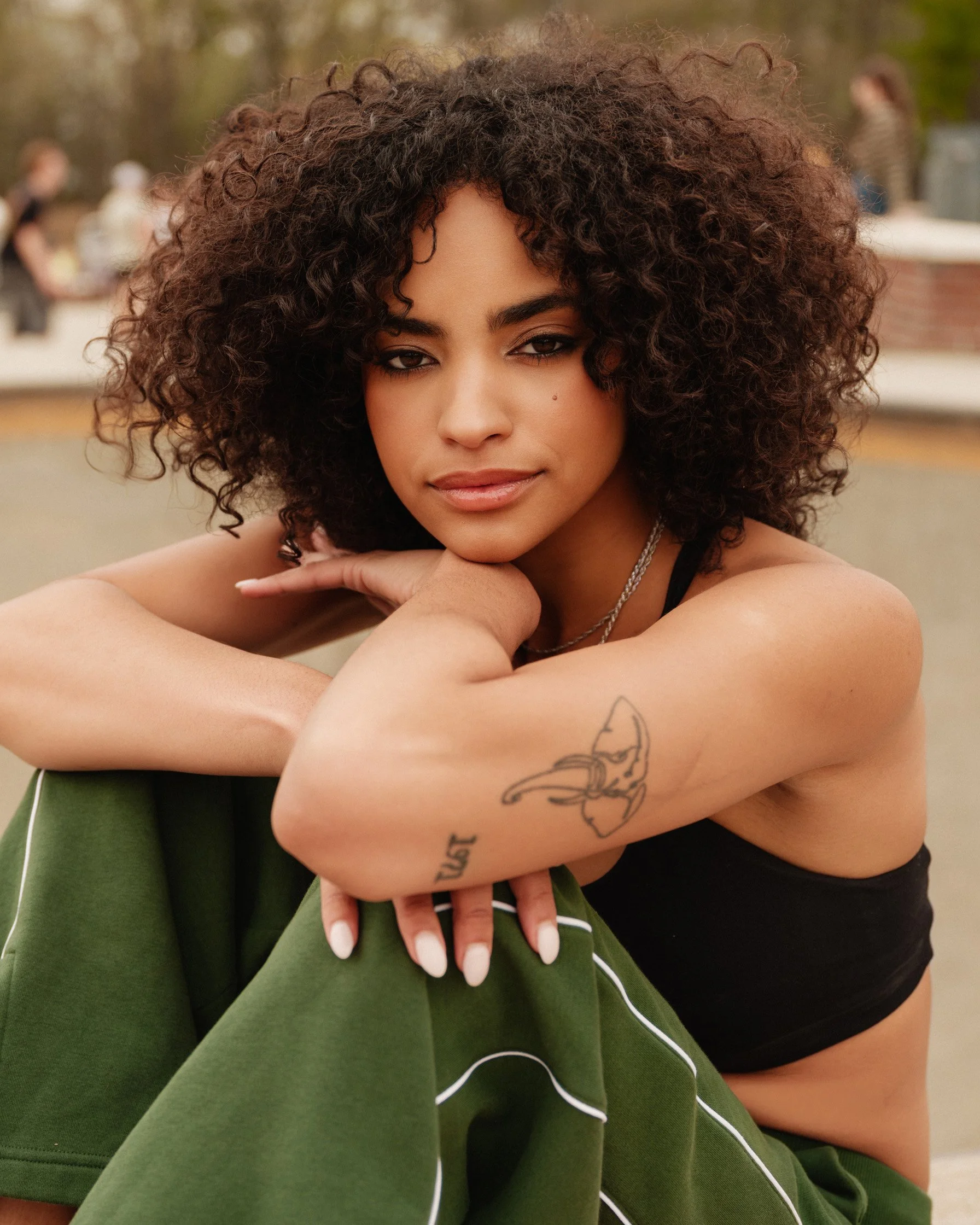 Woman with curly hair in green trousers seated outdoors, fashion portrait | Jon Premosch, fashion and lifestyle photographer
