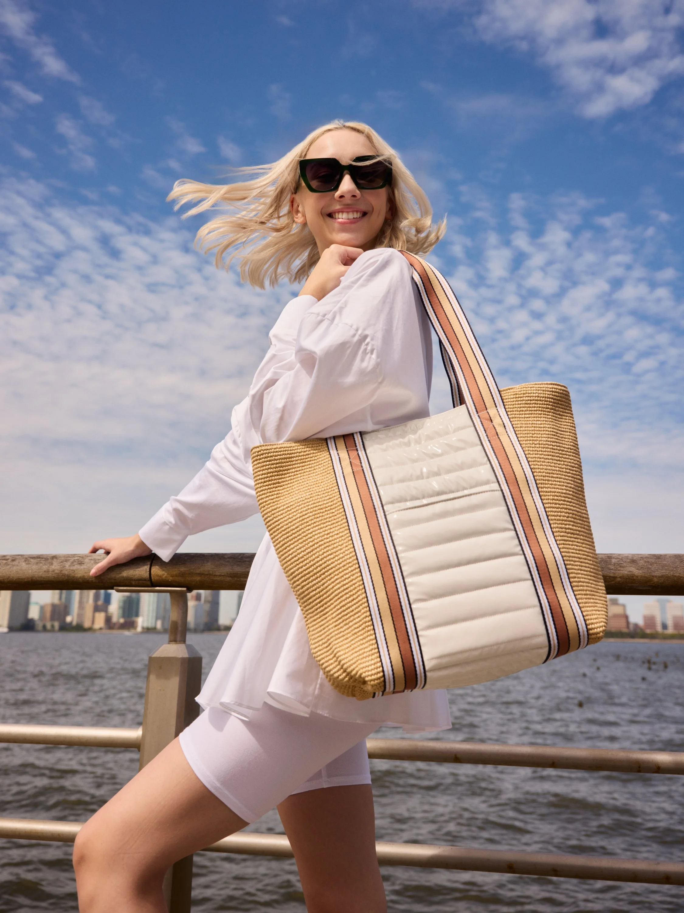 Woman in white carrying a striped Think Royln tote along the New York waterfront, accessories photography for Think Royln | Jon Premosch, fashion and lifestyle photographer