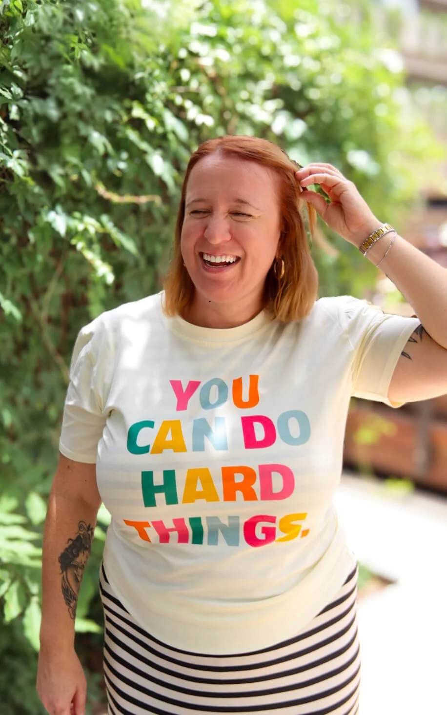 Lisa Osborn, founder of Real Well Therapy, smiling outdoors in a colorful "You Can Do Hard Things" shirt.