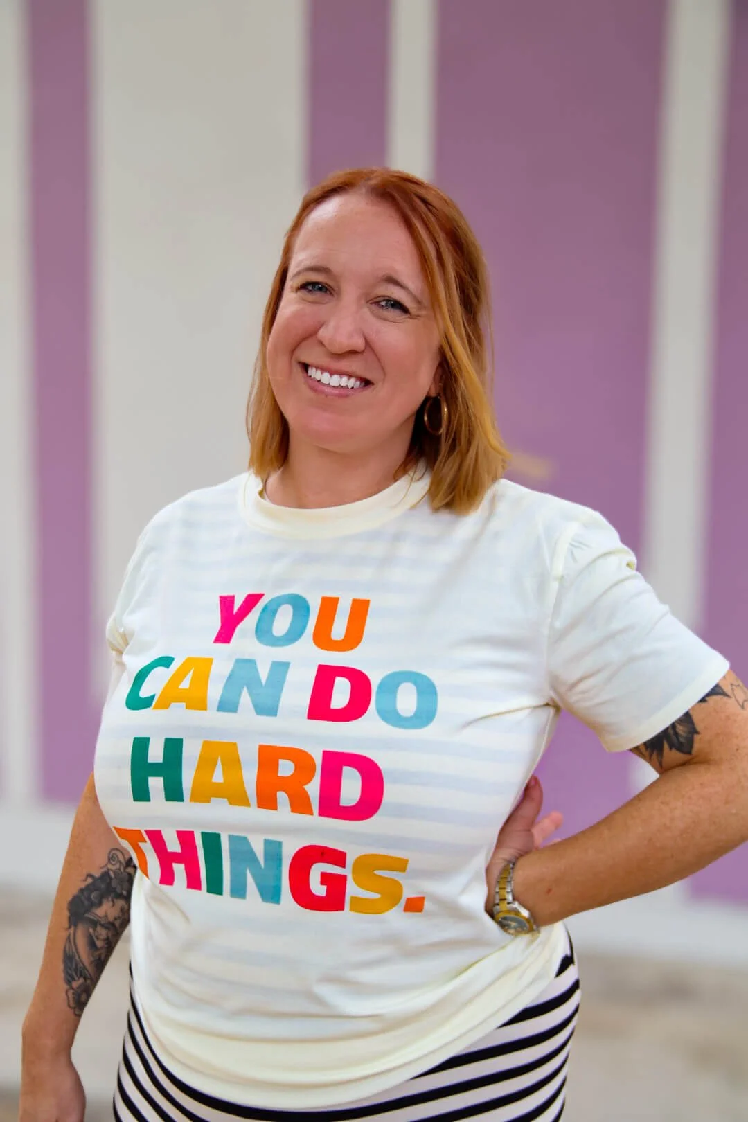 Lisa Osborn, LCSW, EMDR therapist and anxiety therapist, smiling in front of a striped lavender wall while wearing a colorful "You Can Do Hard Things" shirt.
