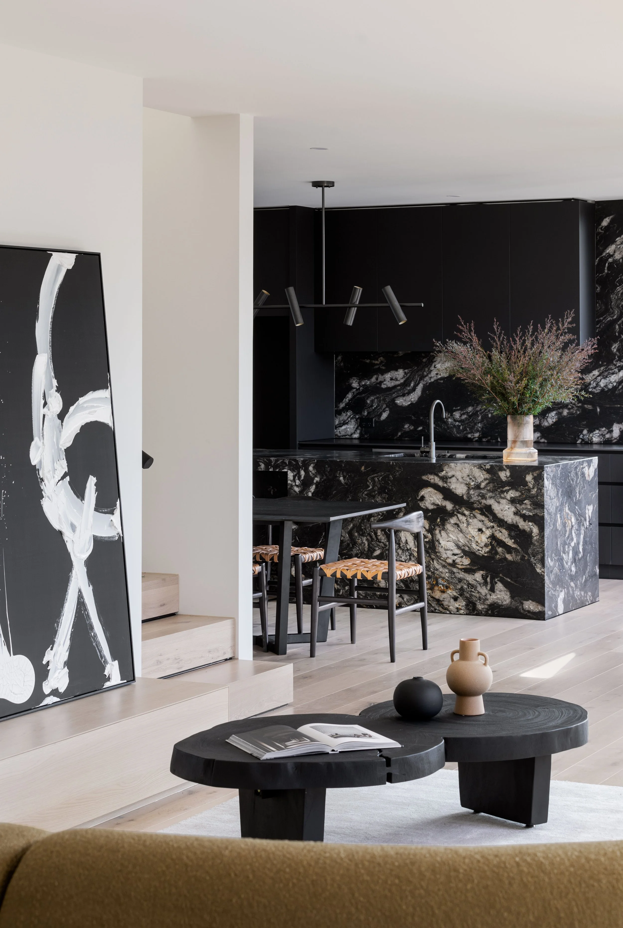 Modern kitchen and living room with black and white decor, black abstract art leaning against wall, black coffee table with decorative vases, and dining area with black table and chairs.