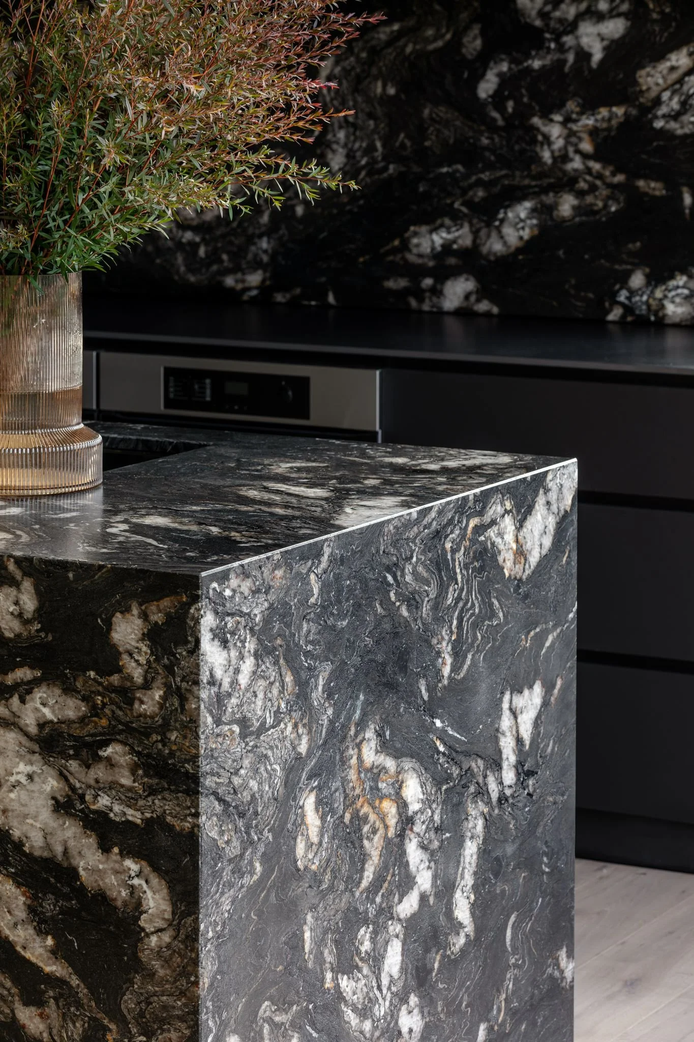 Close-up of a black and white marble countertop and island with a potted plant on top in a modern kitchen.