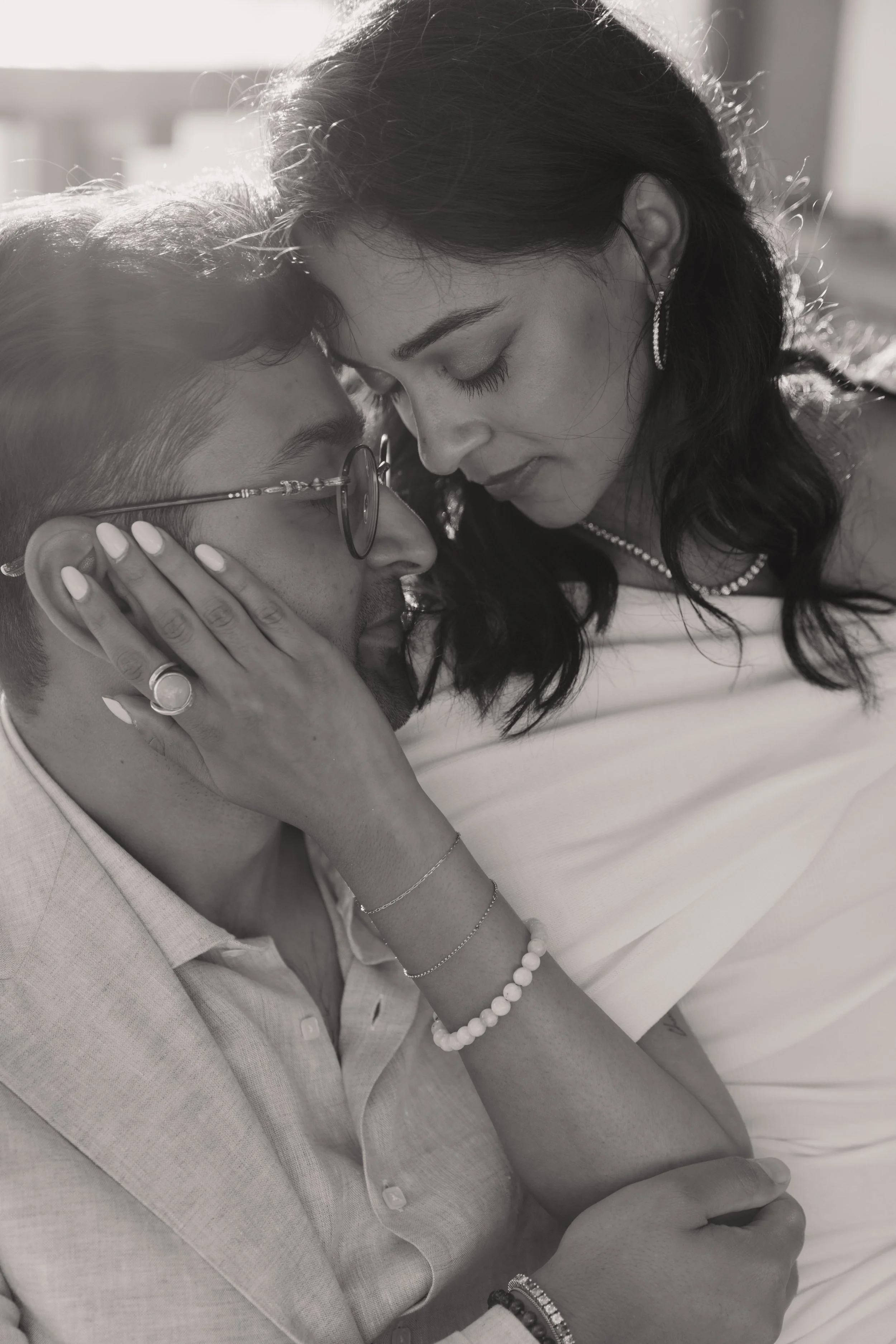 A black and white photo of a couple with their foreheads touching, holding each other's faces tenderly.