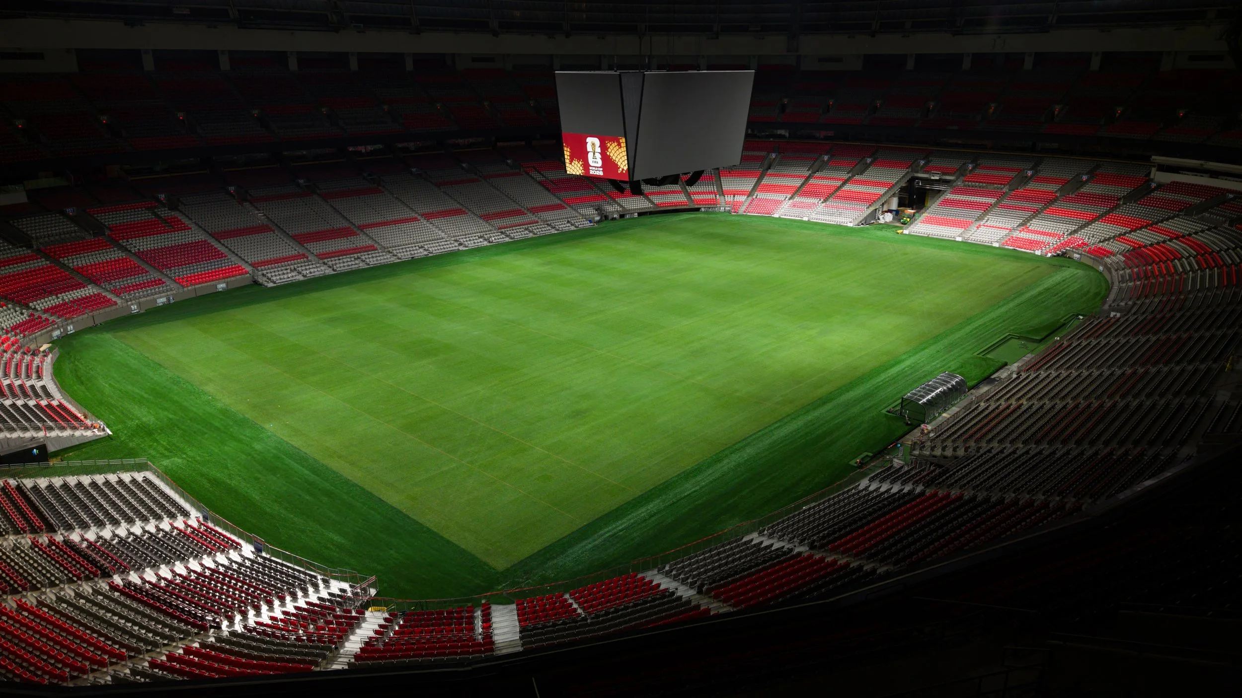 Empty soccer stadium with green field and red and gray seats.