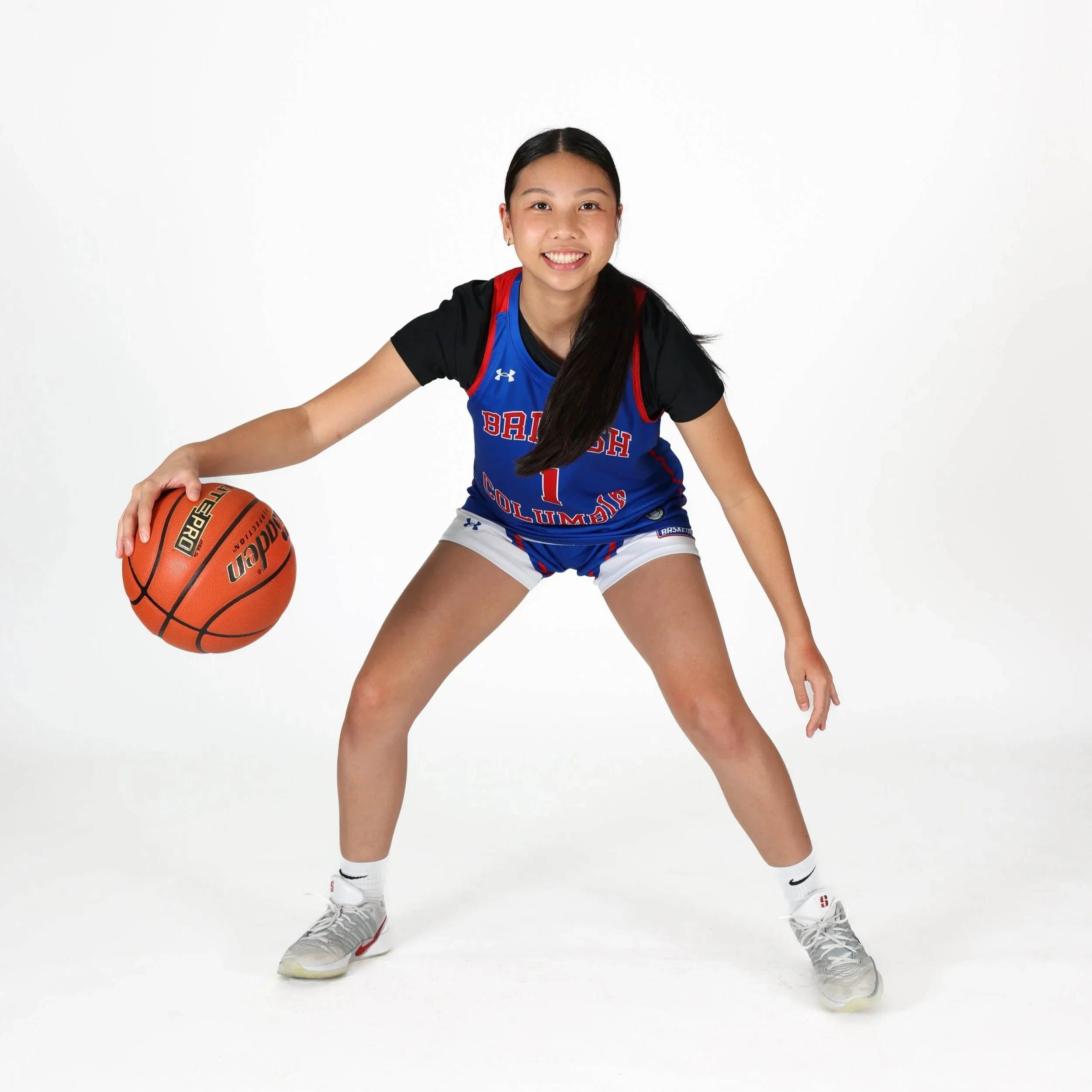 A young woman in a basketball uniform dribbling a basketball on a white background.