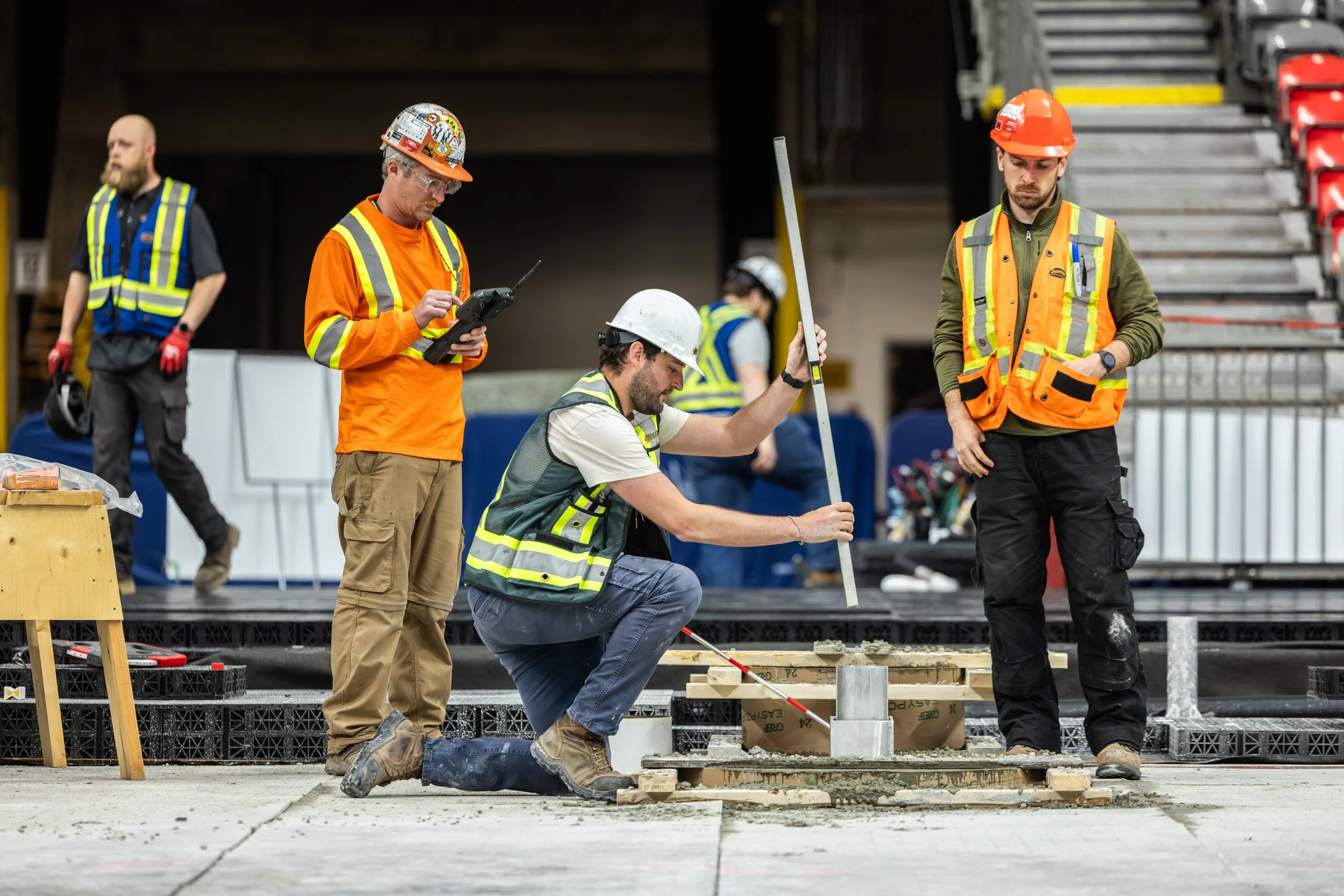 Construction workers in safety vests and helmets working on a concrete foundation with tools and equipment around them.