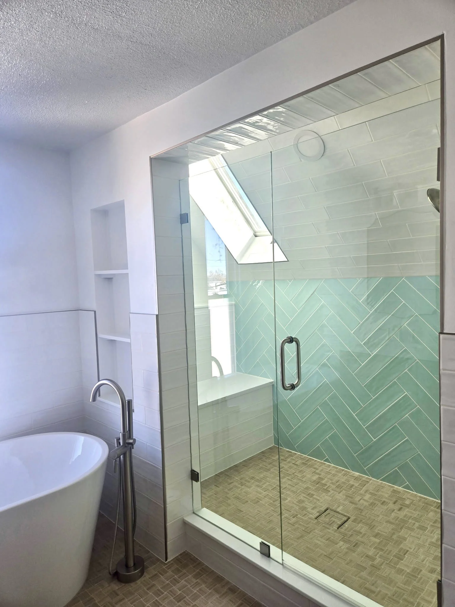 Colorado bathroom remodel with glass walk-in shower, aqua herringbone tile, skylight, and freestanding soaking tub