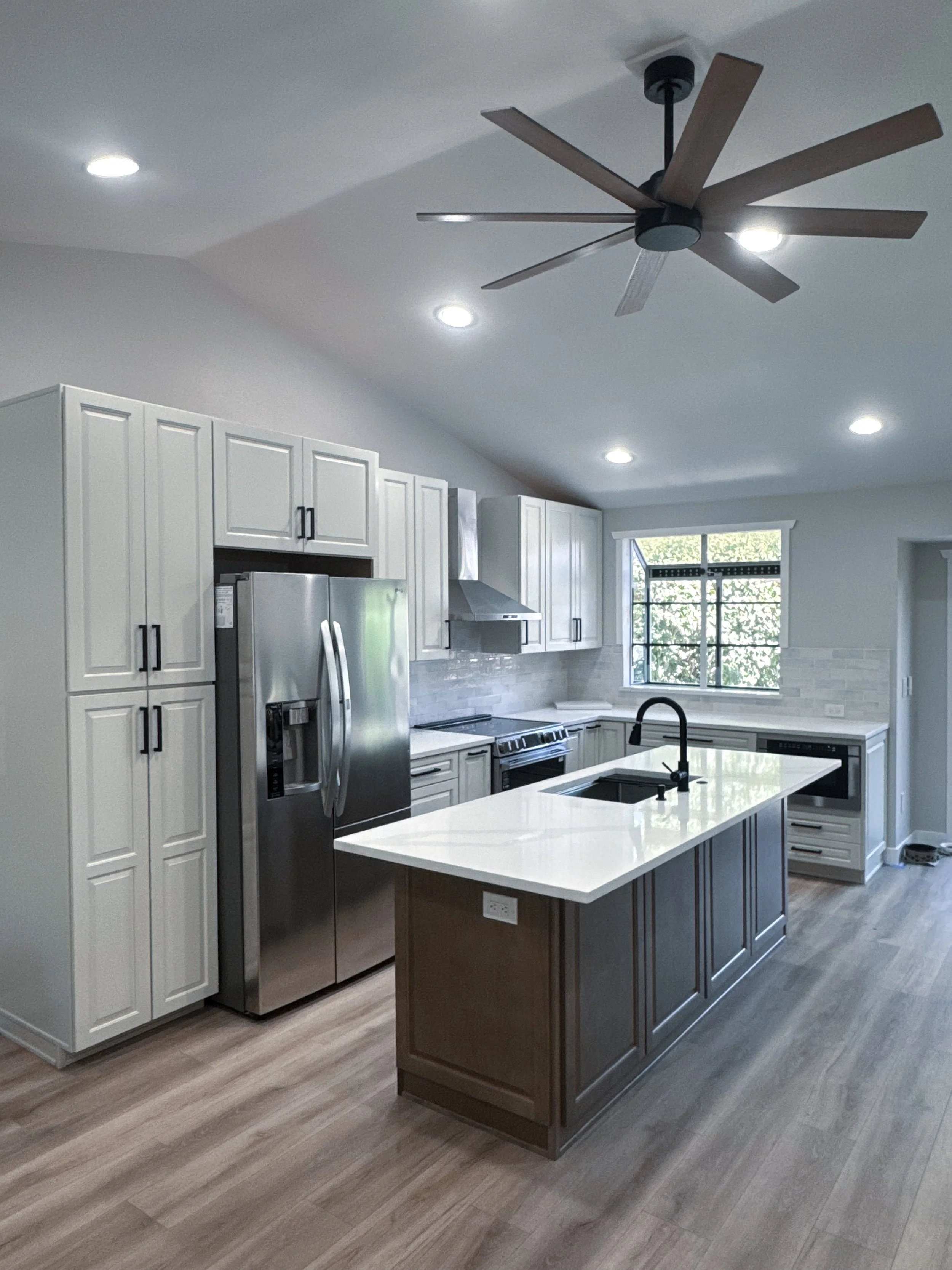 Modern kitchen with white cabinets, stainless steel refrigerator, black faucet, island with white countertop, and hardwood flooring.