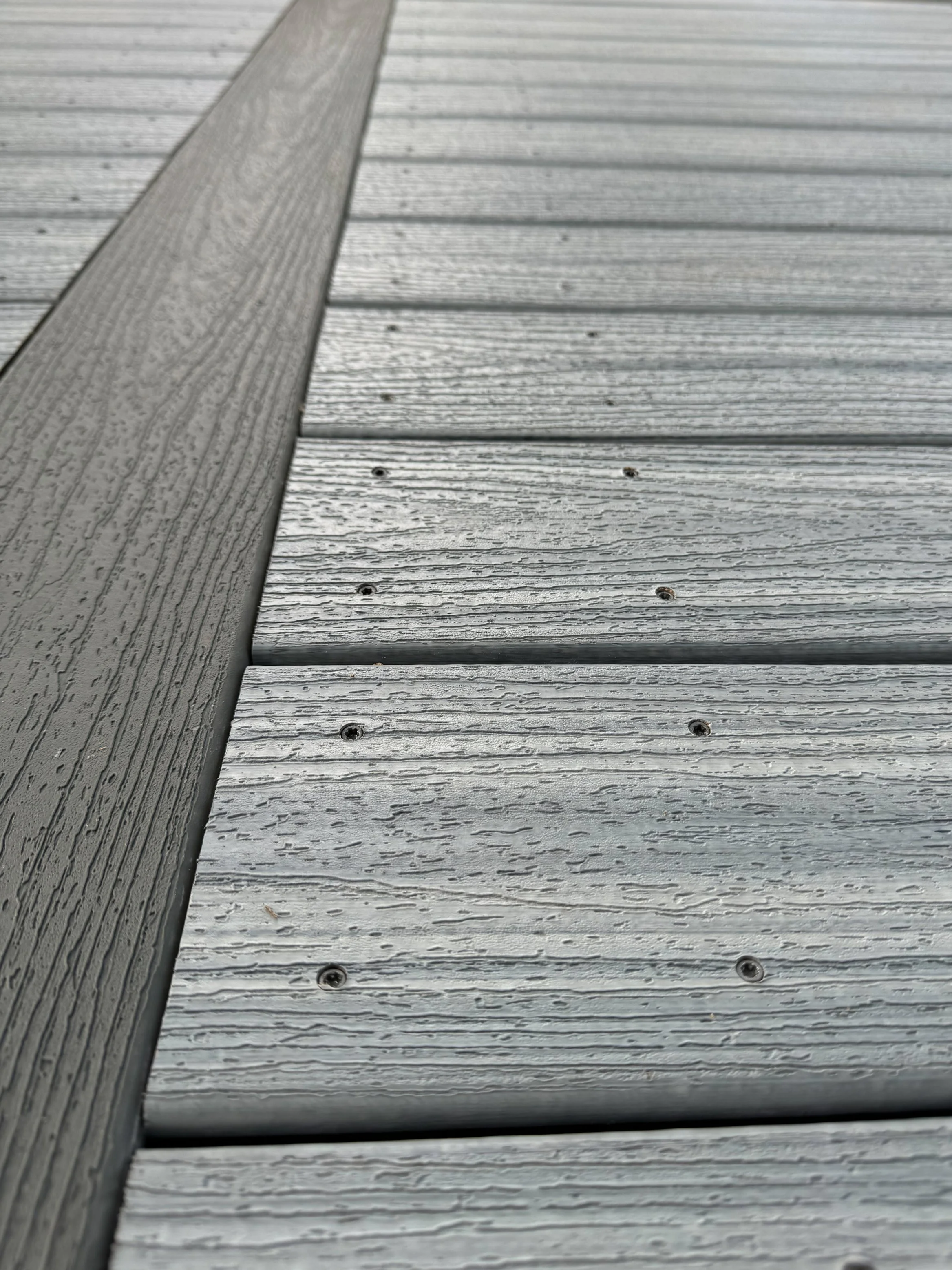 Close-up view of wooden planks with visible grain and screws, arranged horizontally on a building or deck.