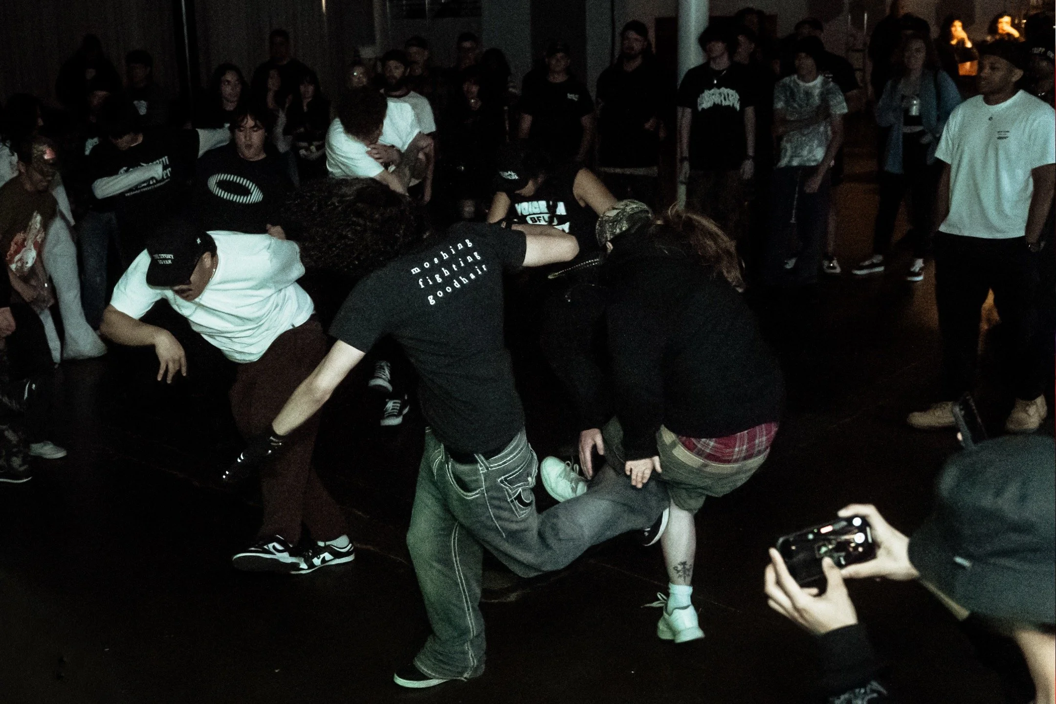 Group of people at a dance or music event, some practicing breakdancing moves, with a crowd watching in the background.