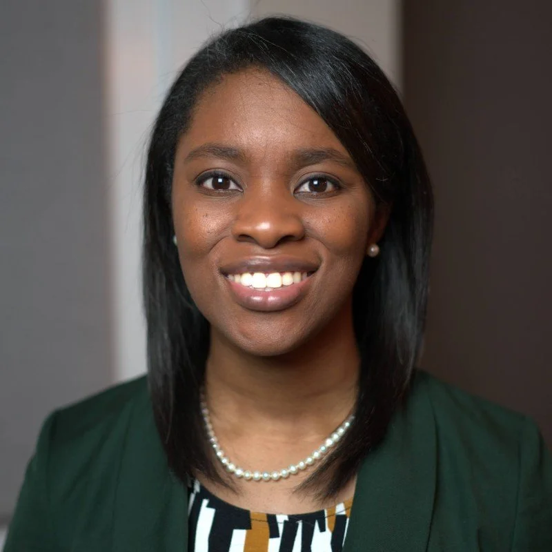 Headshot of Dr. Ugochi Okoroafor, double board-certified orthopedic surgeon and founder of Niche Hand Surgery and MD Independent, wearing a dark green blazer, patterned top, pearl necklace and earrings, smiling confidently.