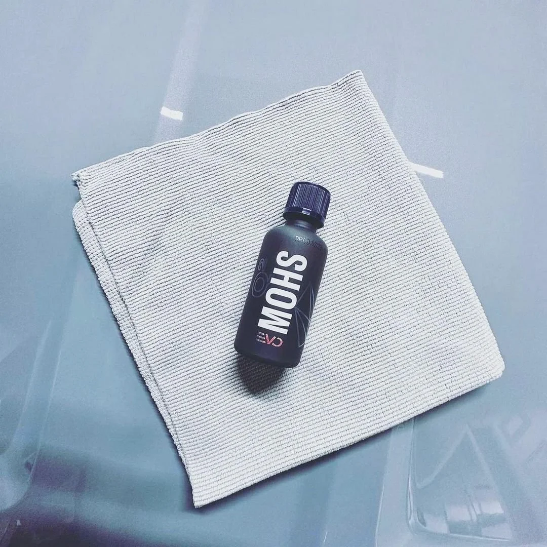 A black bottle labeled 'SHOWER' resting on a white textured washcloth on a smooth surface.