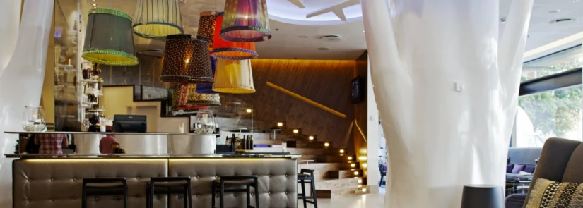 Modern bar interior with eclectic hanging lamps and wooden staircase.